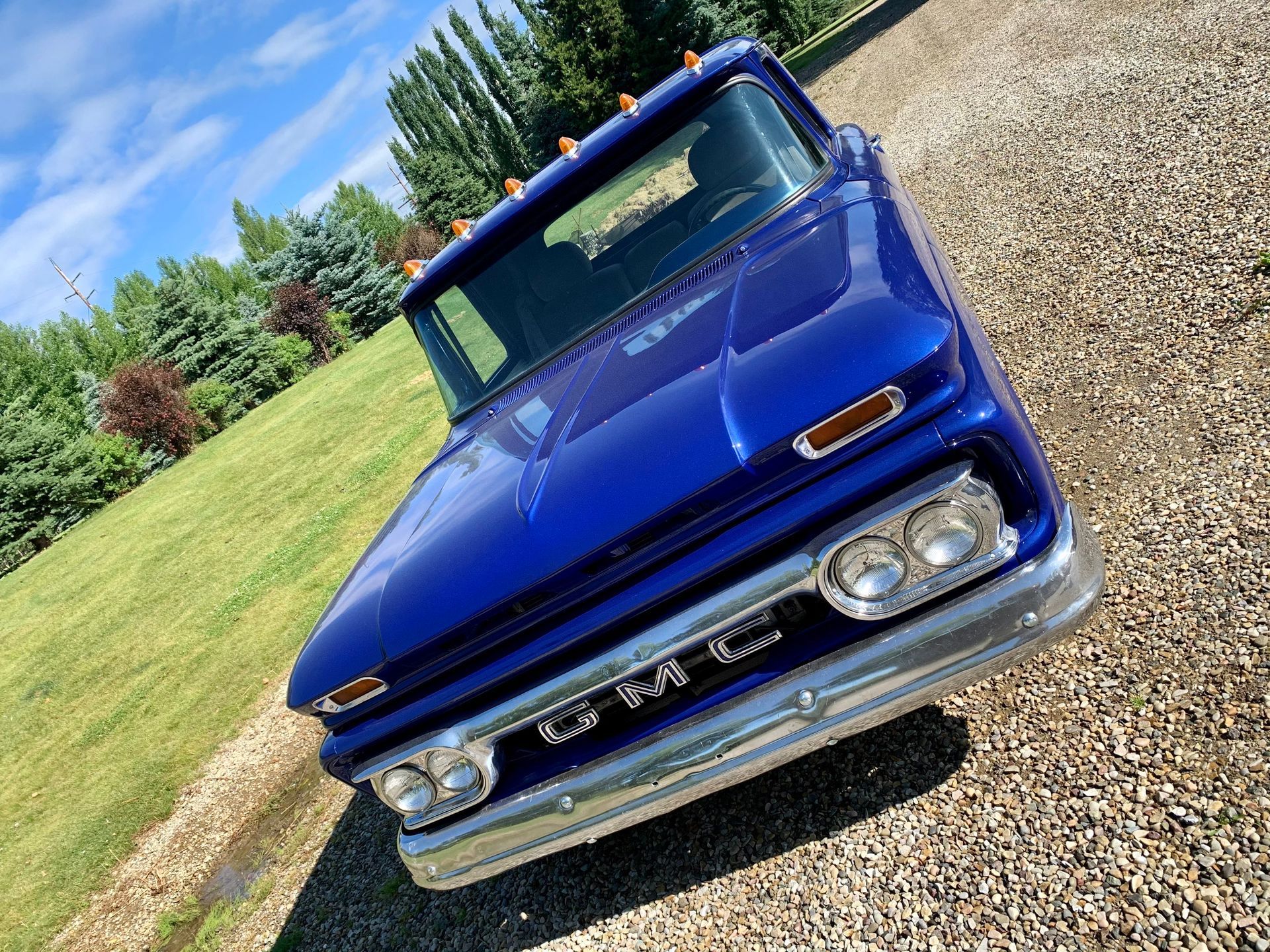 A blue gmc truck is parked on a gravel road.