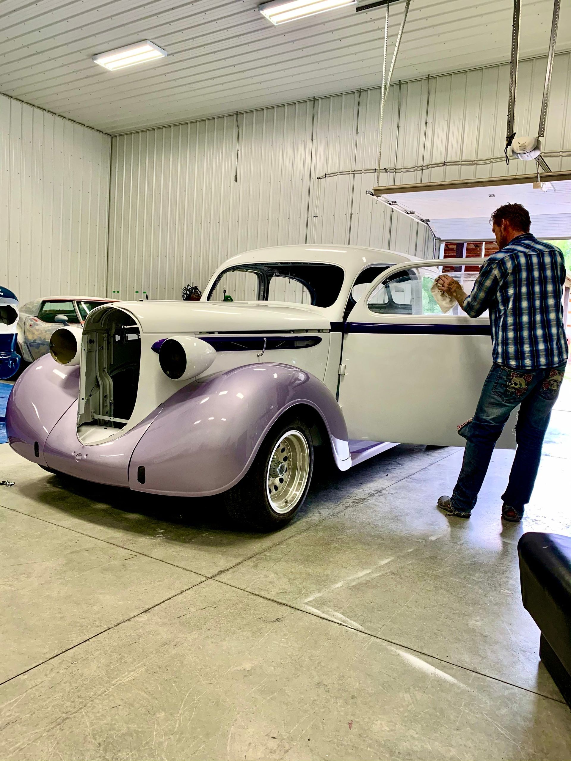 A man is standing next to a purple and white car in a garage.