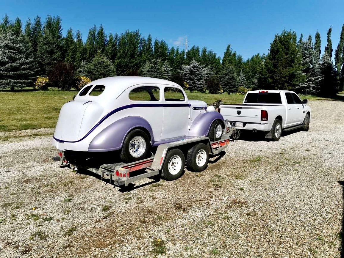 A white truck is towing a purple car on a trailer.