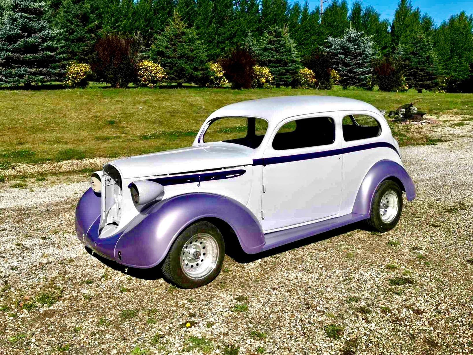A white and purple car is parked on a gravel road.