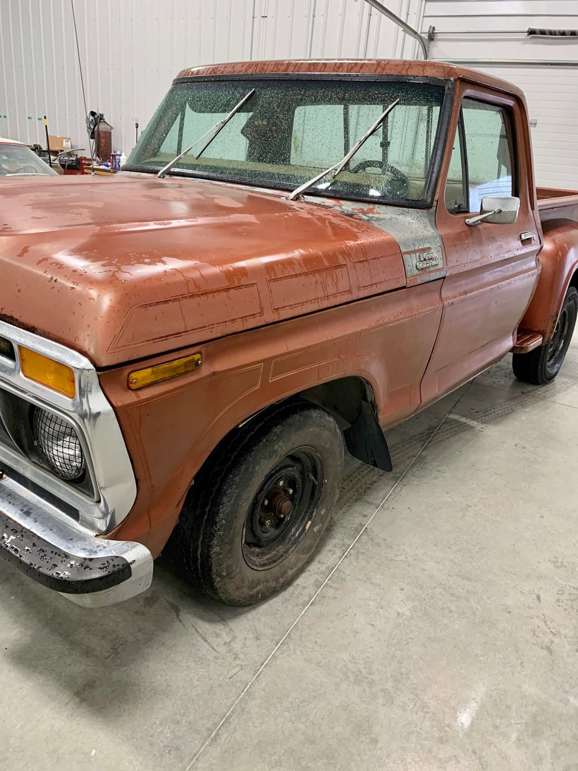 An old rusty pickup truck is parked in a garage.