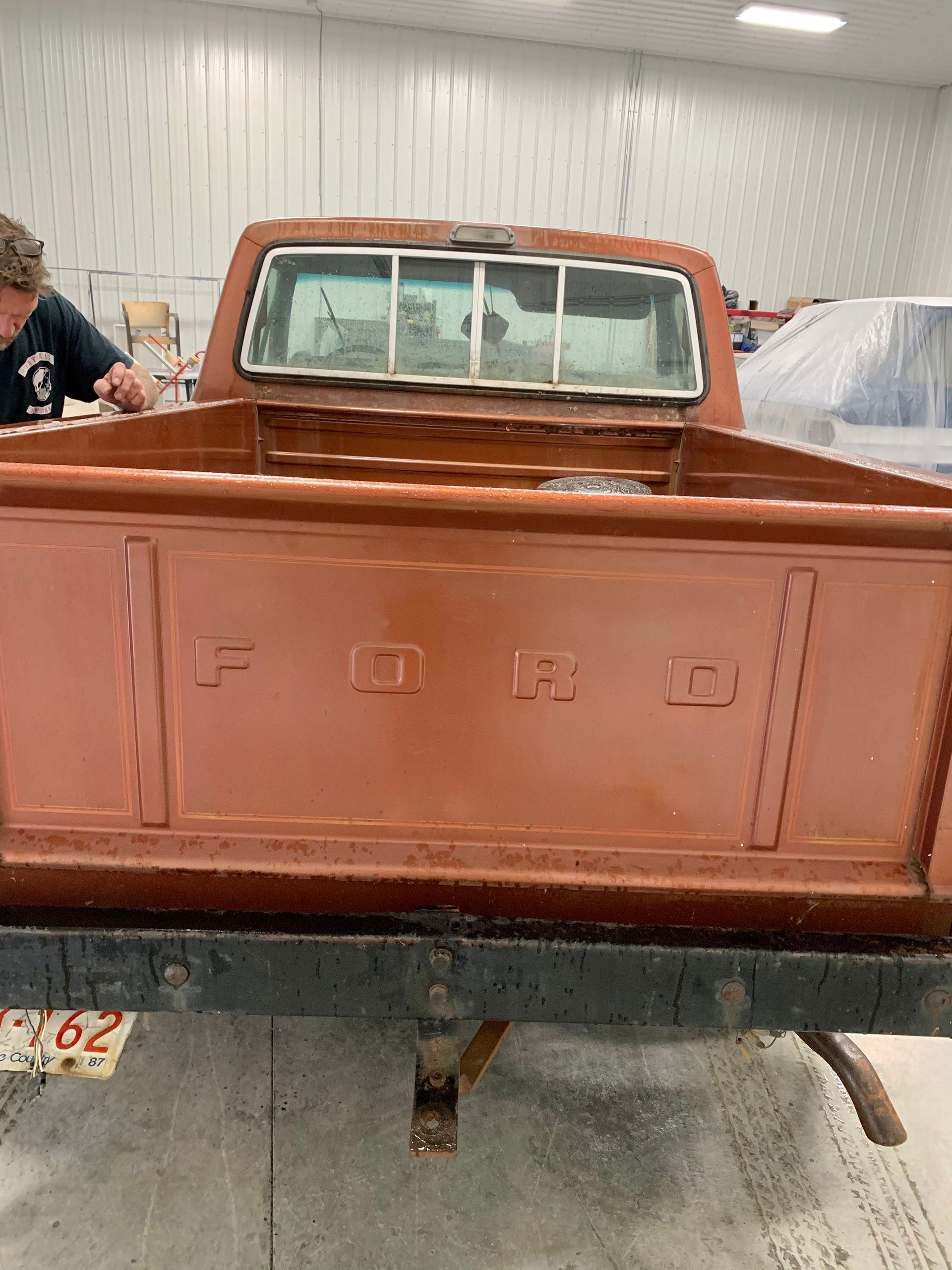 A man is working on the back of a ford truck in a garage.