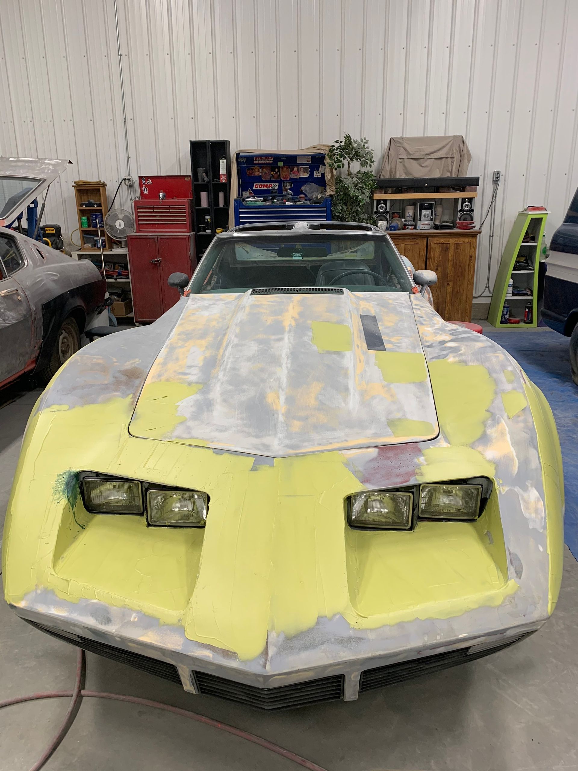 A yellow corvette is being painted in a garage.