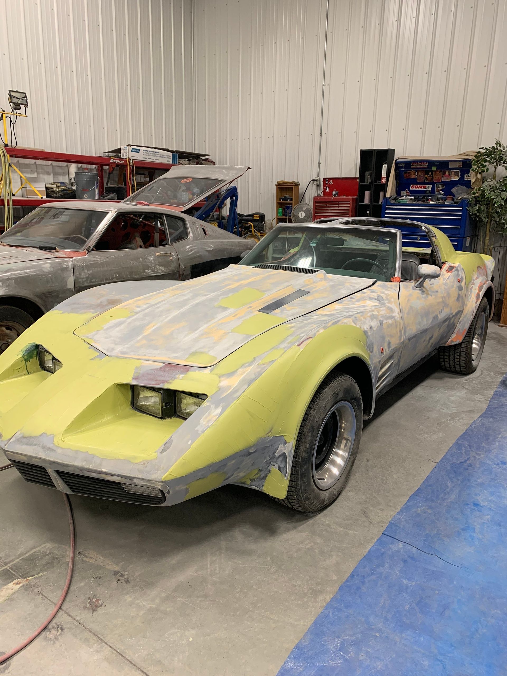 A yellow corvette is sitting in a garage with other cars.