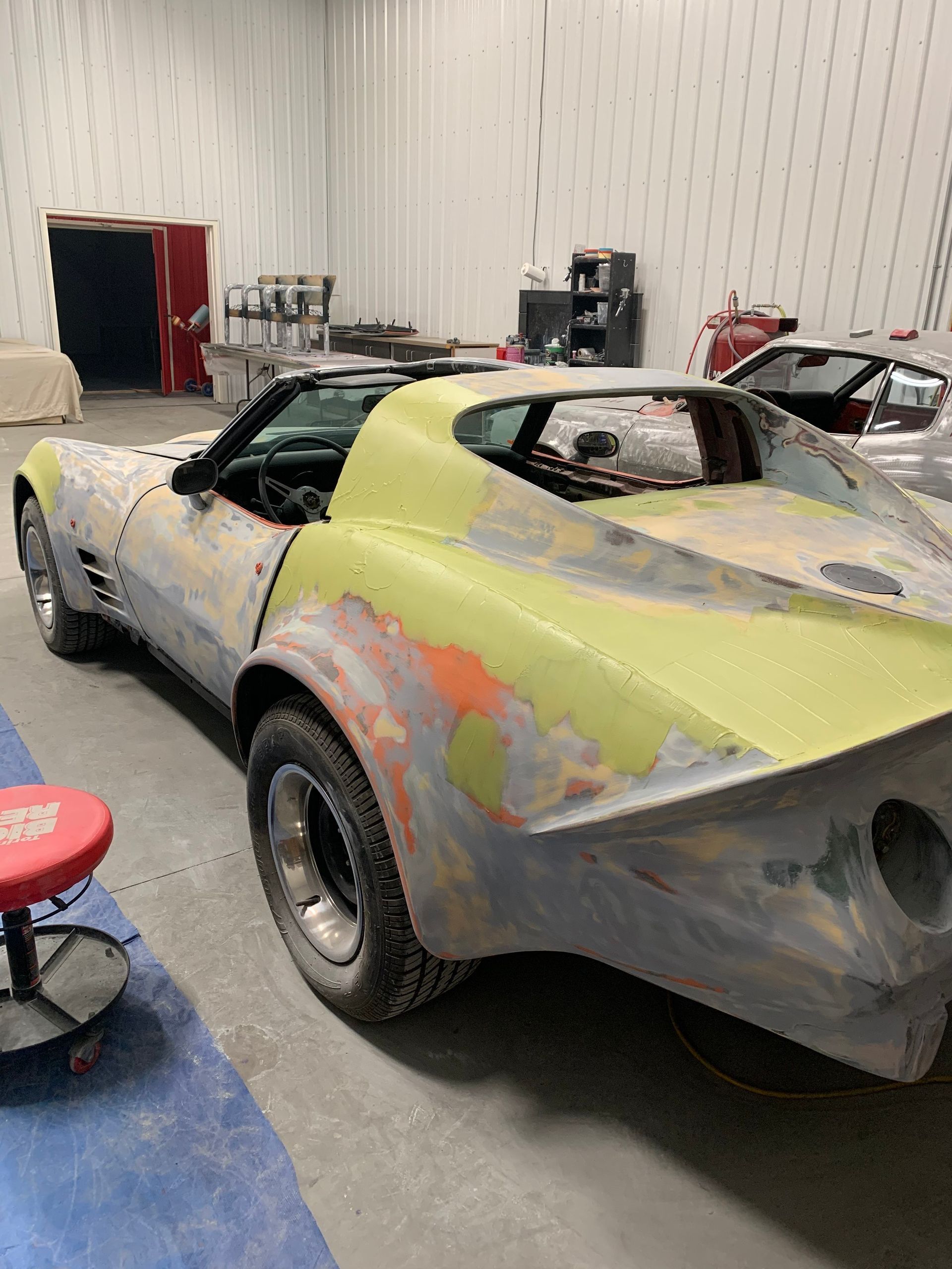 A yellow corvette is being restored in a garage.