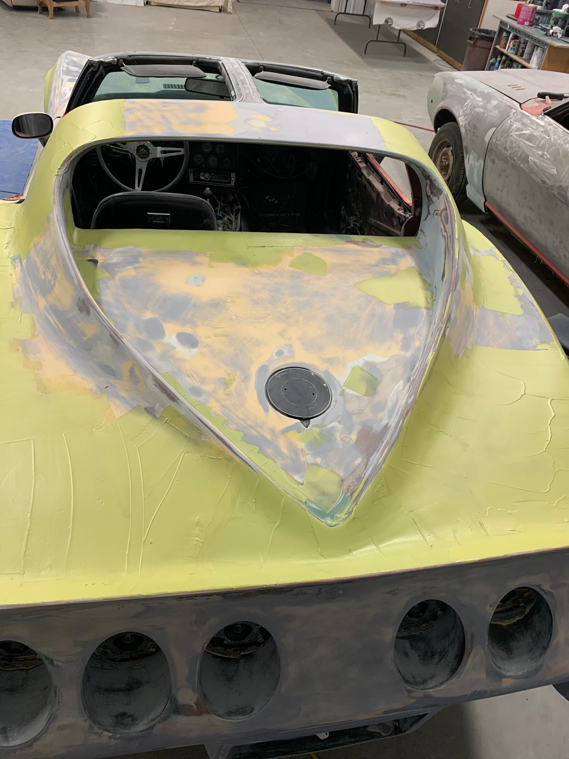 A yellow corvette is being restored in a garage.
