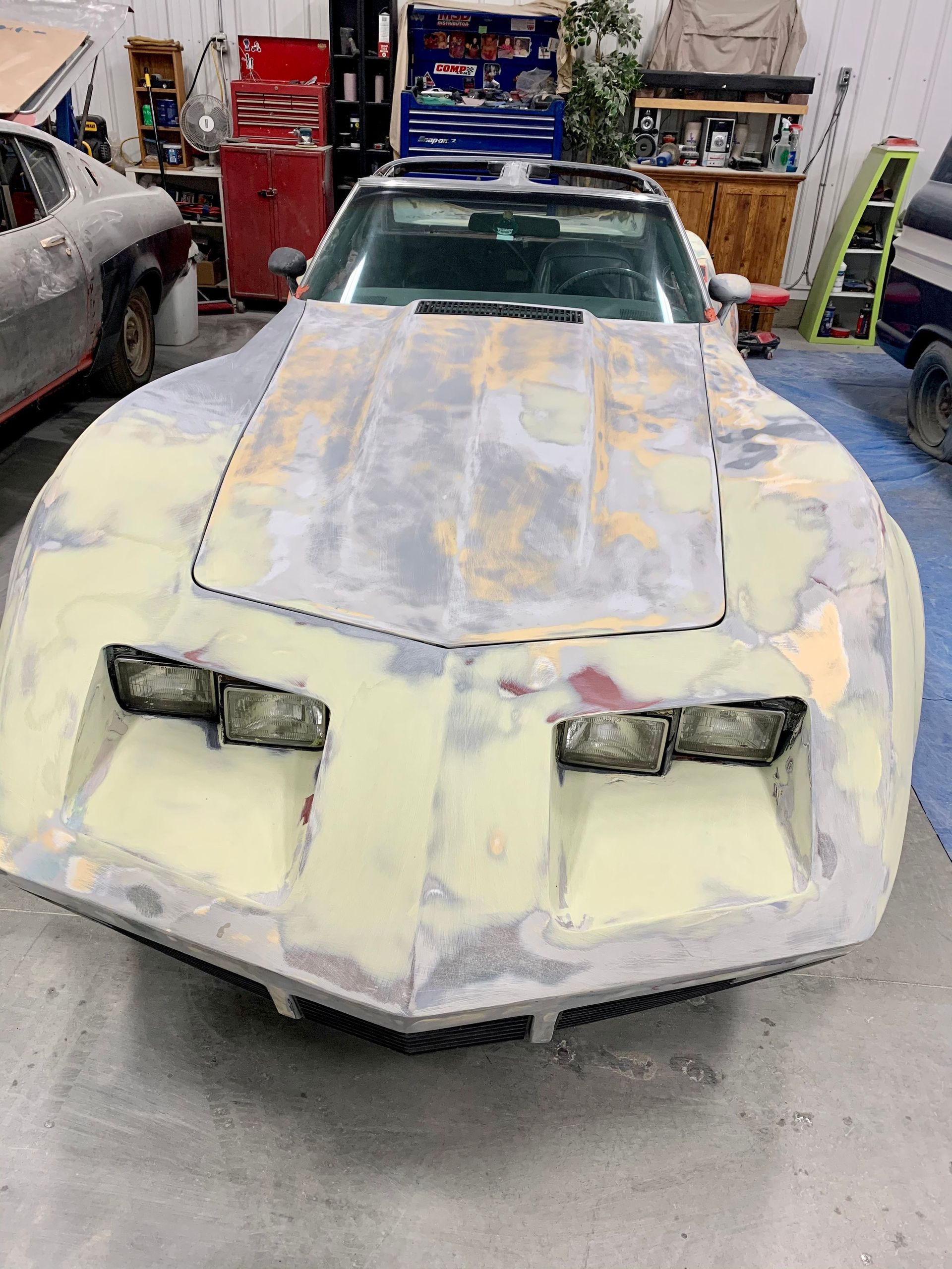A white corvette is being restored in a garage.