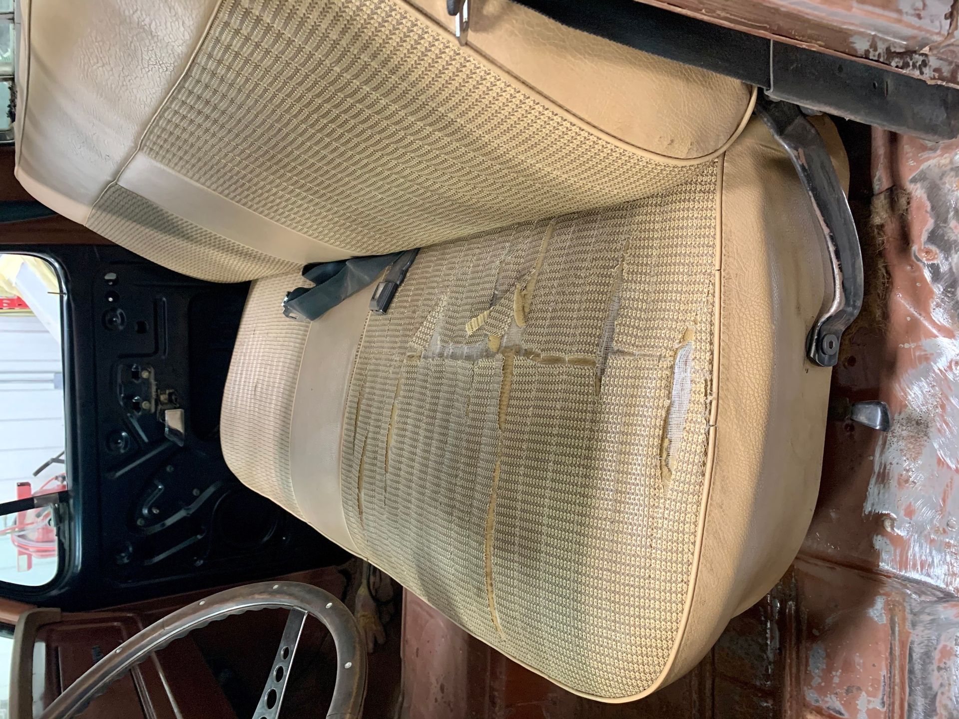A close up of a car seat with a steering wheel in the background.