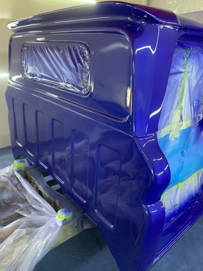 A blue truck is being painted in a garage.