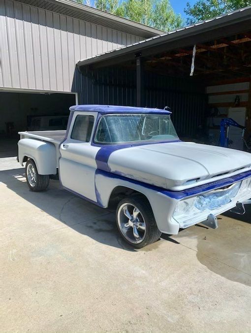 A white and blue truck is parked in front of a garage.