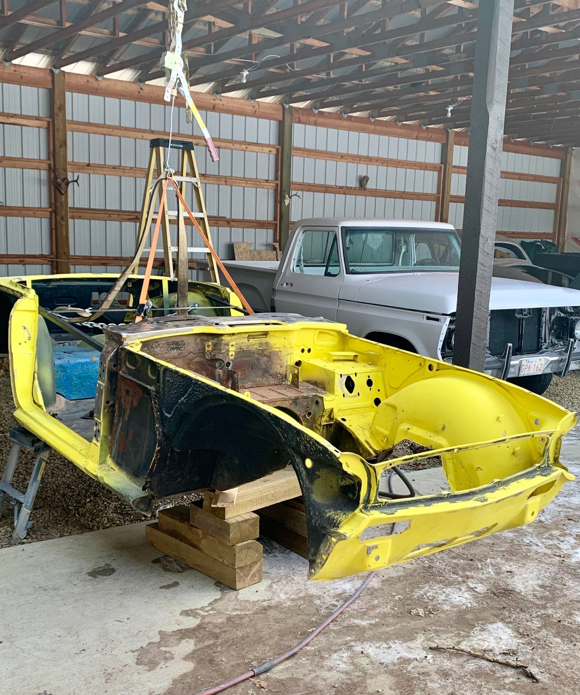 A yellow car is sitting in a barn with a ladder hanging from the ceiling.