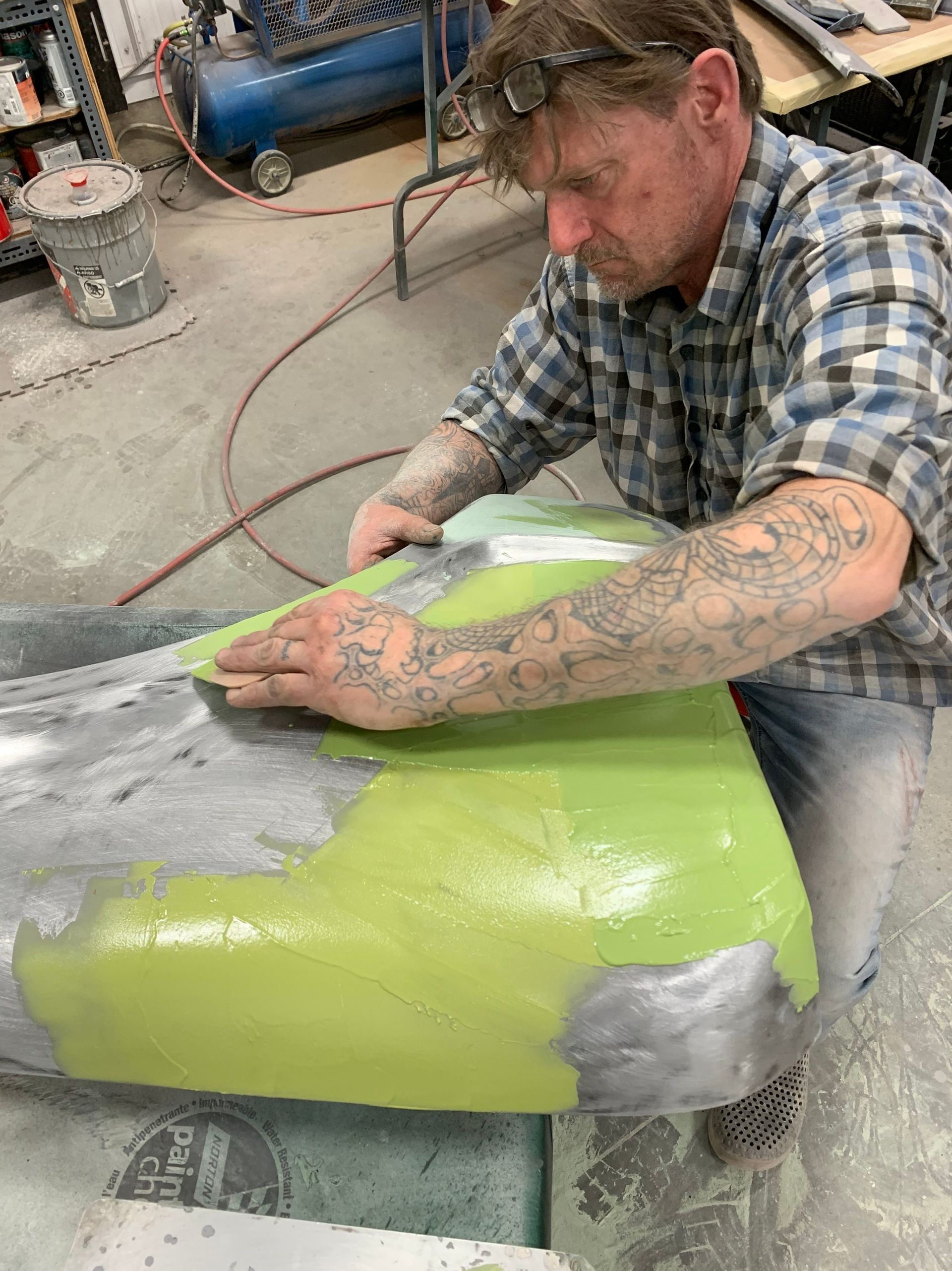 A man is working on a green piece of plastic in a garage.