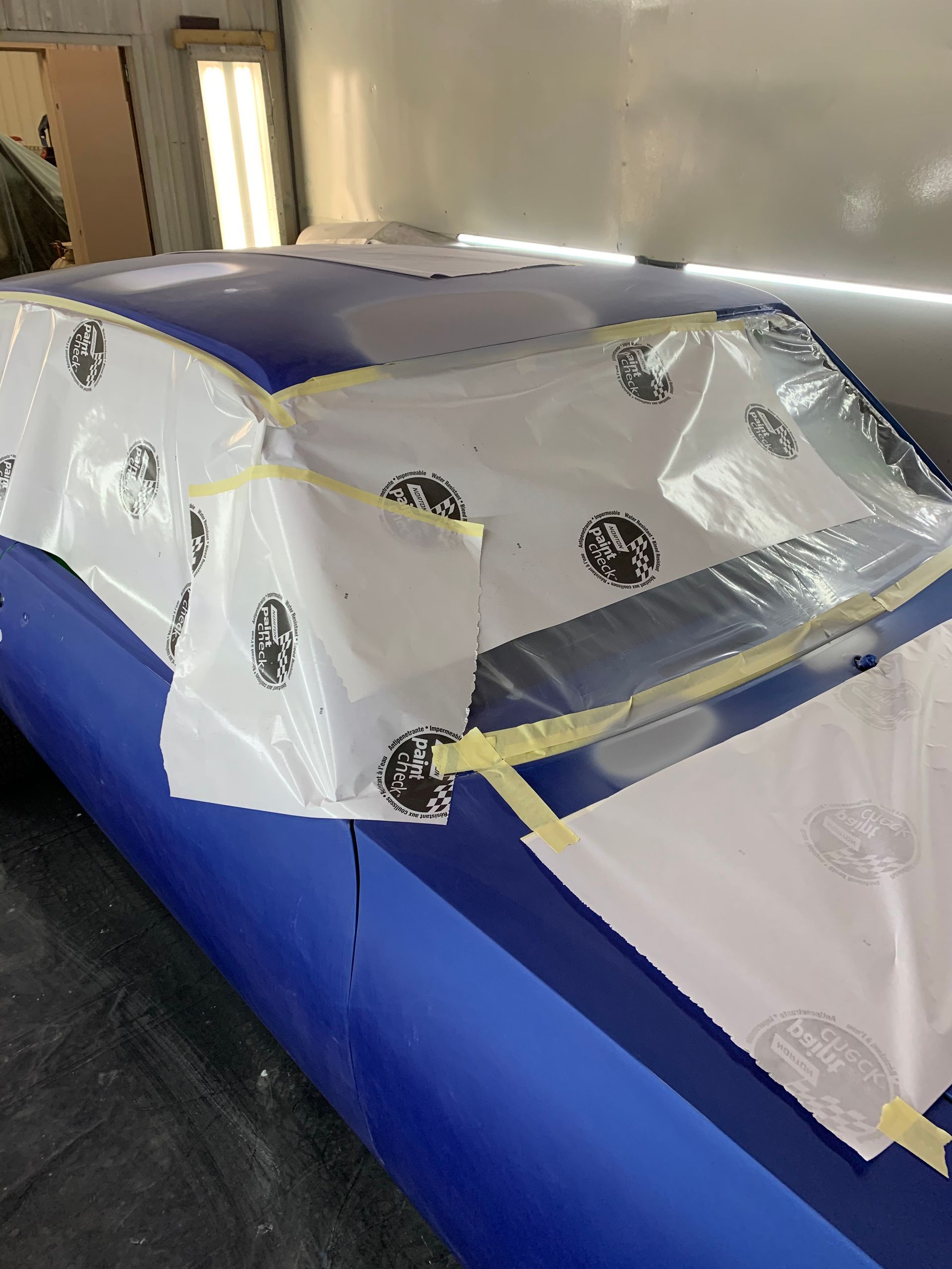 A blue car is covered in plastic and tape in a garage.