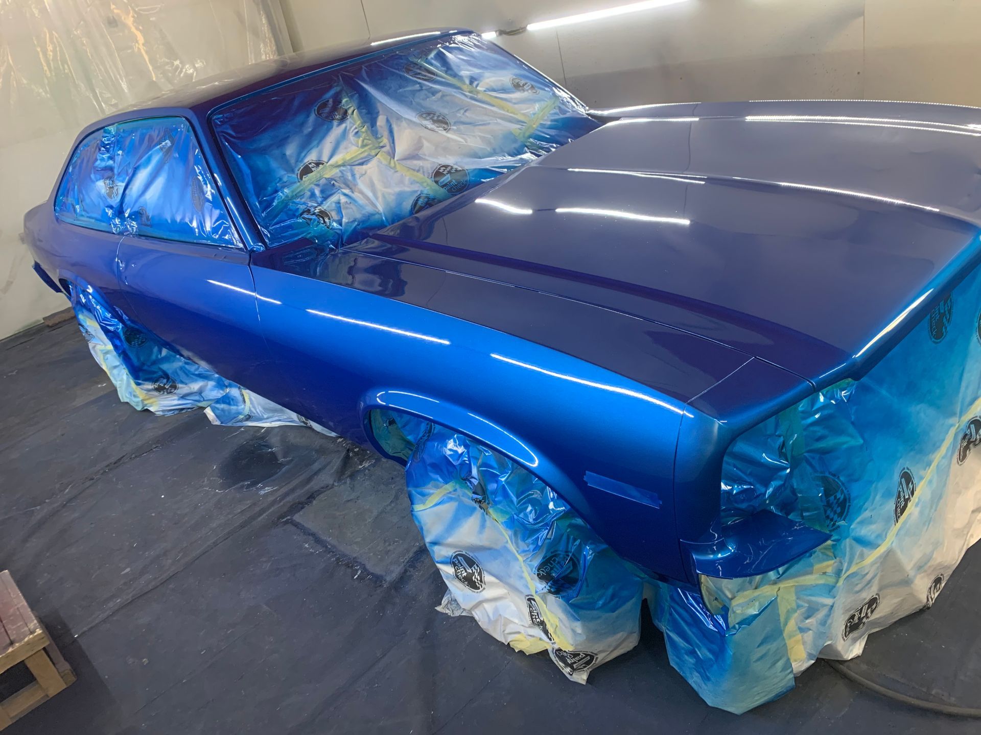 A blue car is being painted in a paint booth.