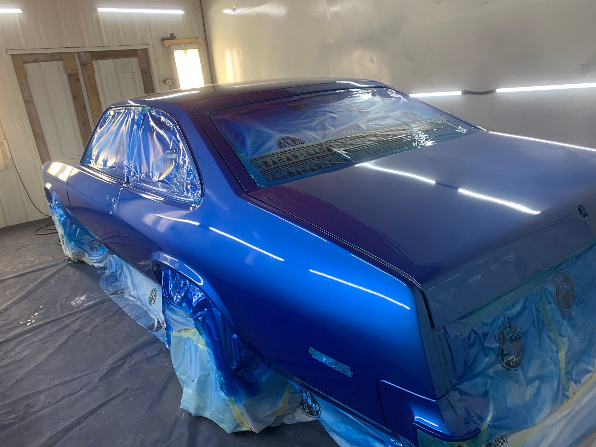 A blue car is being painted in a paint booth.