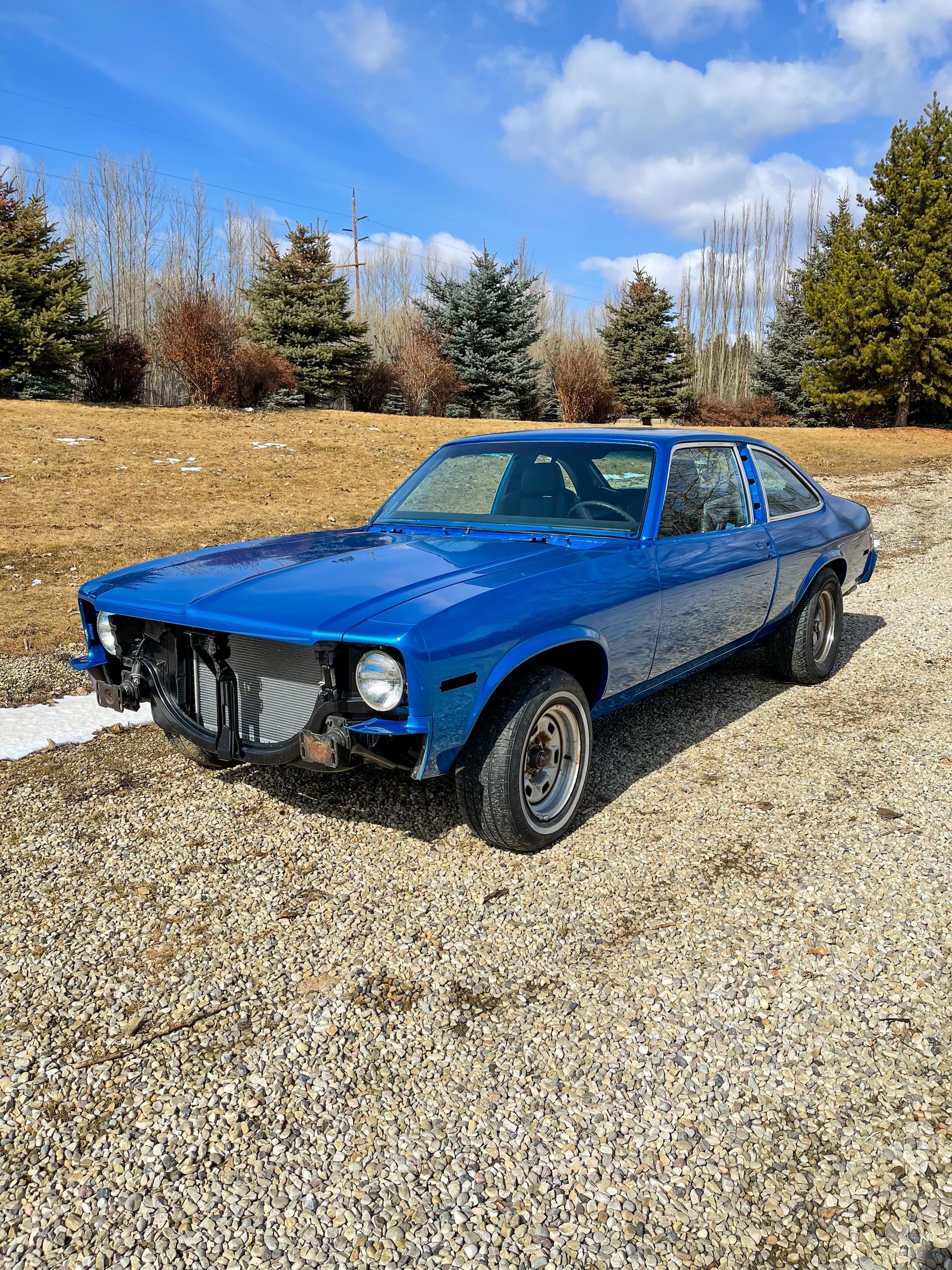 A blue car is parked on a gravel road.