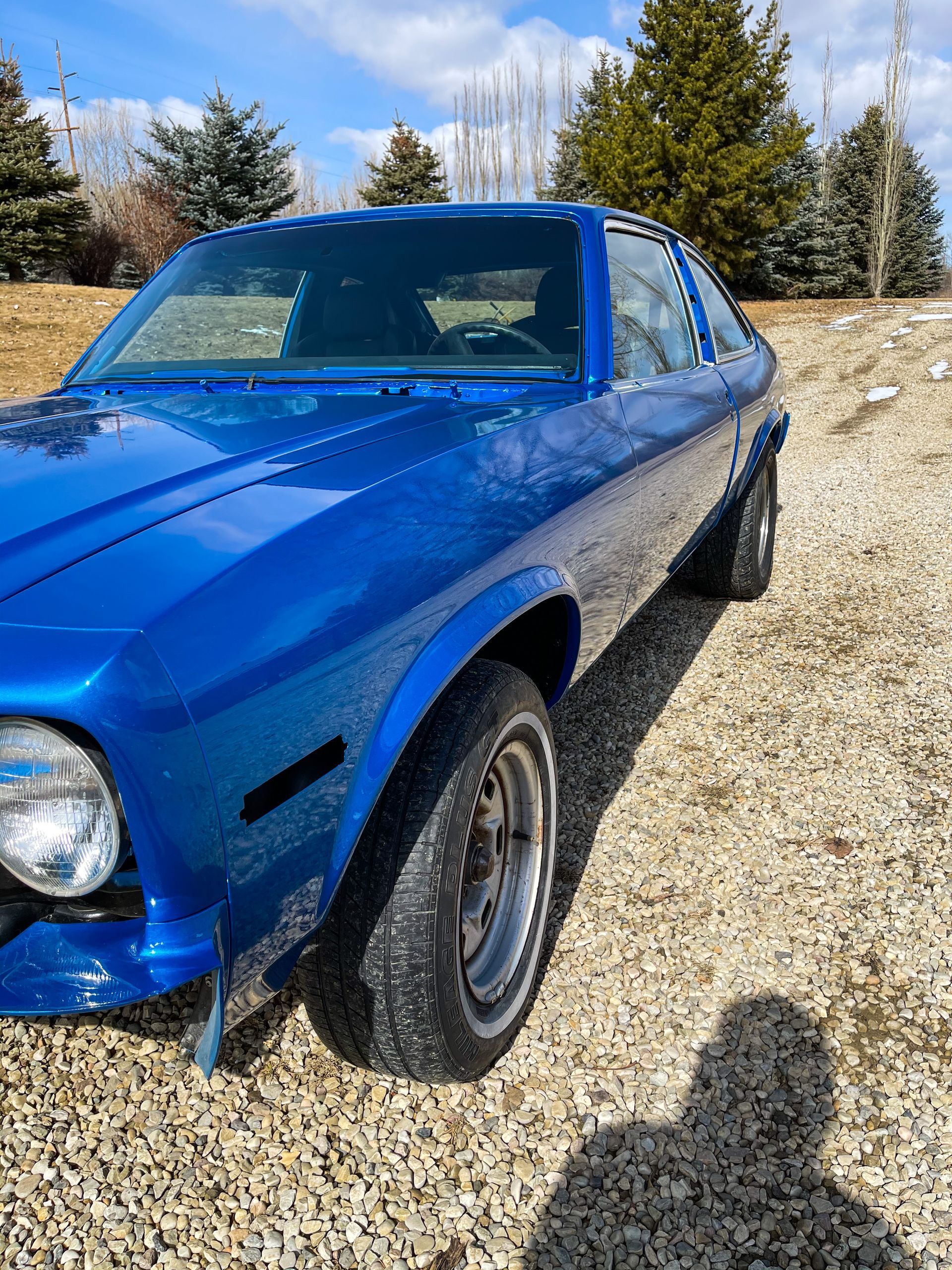 A blue car is parked on a gravel road.