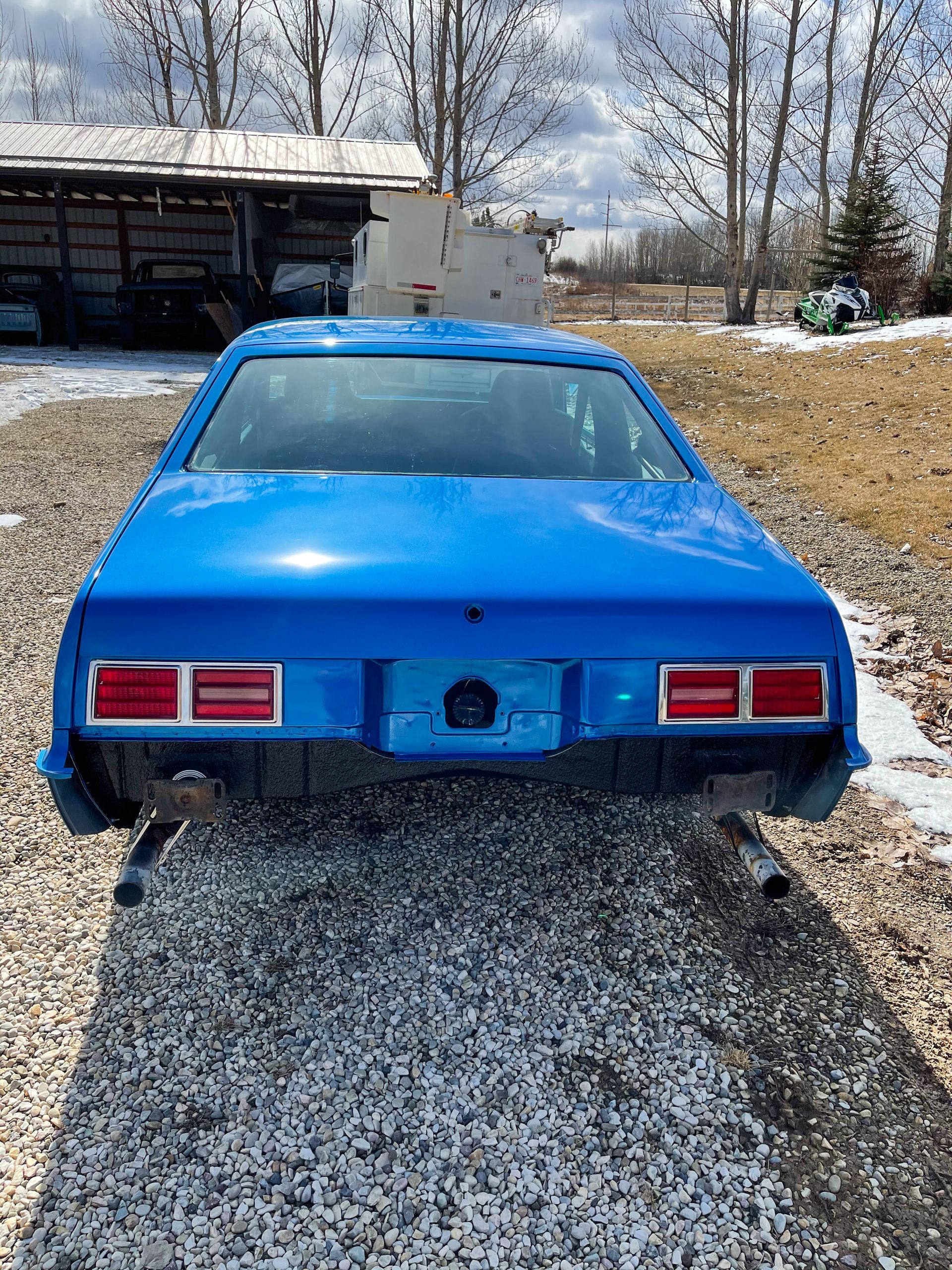 A blue car is parked on a gravel road.