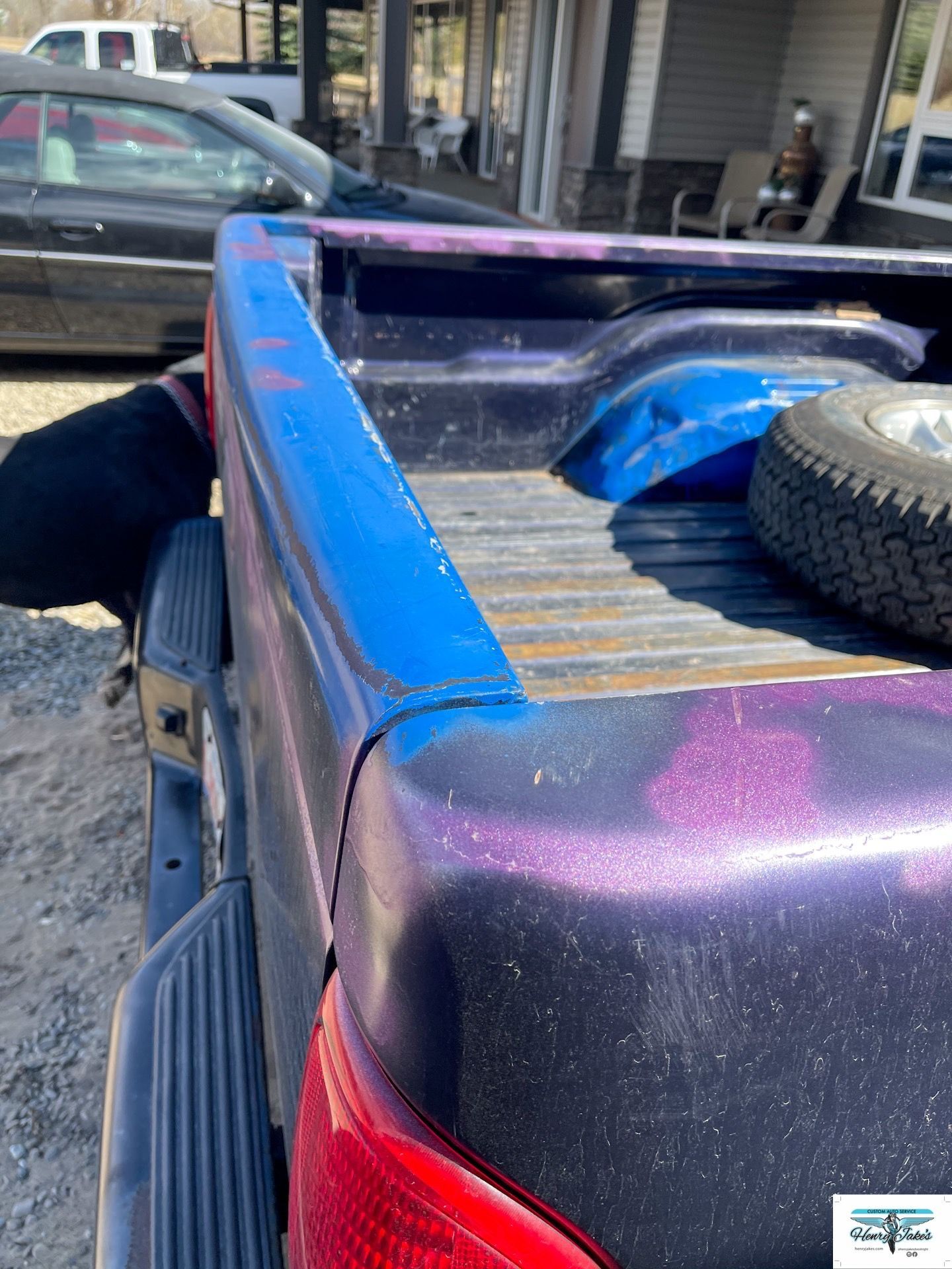 A purple truck with a blue tailgate is parked in front of a house.