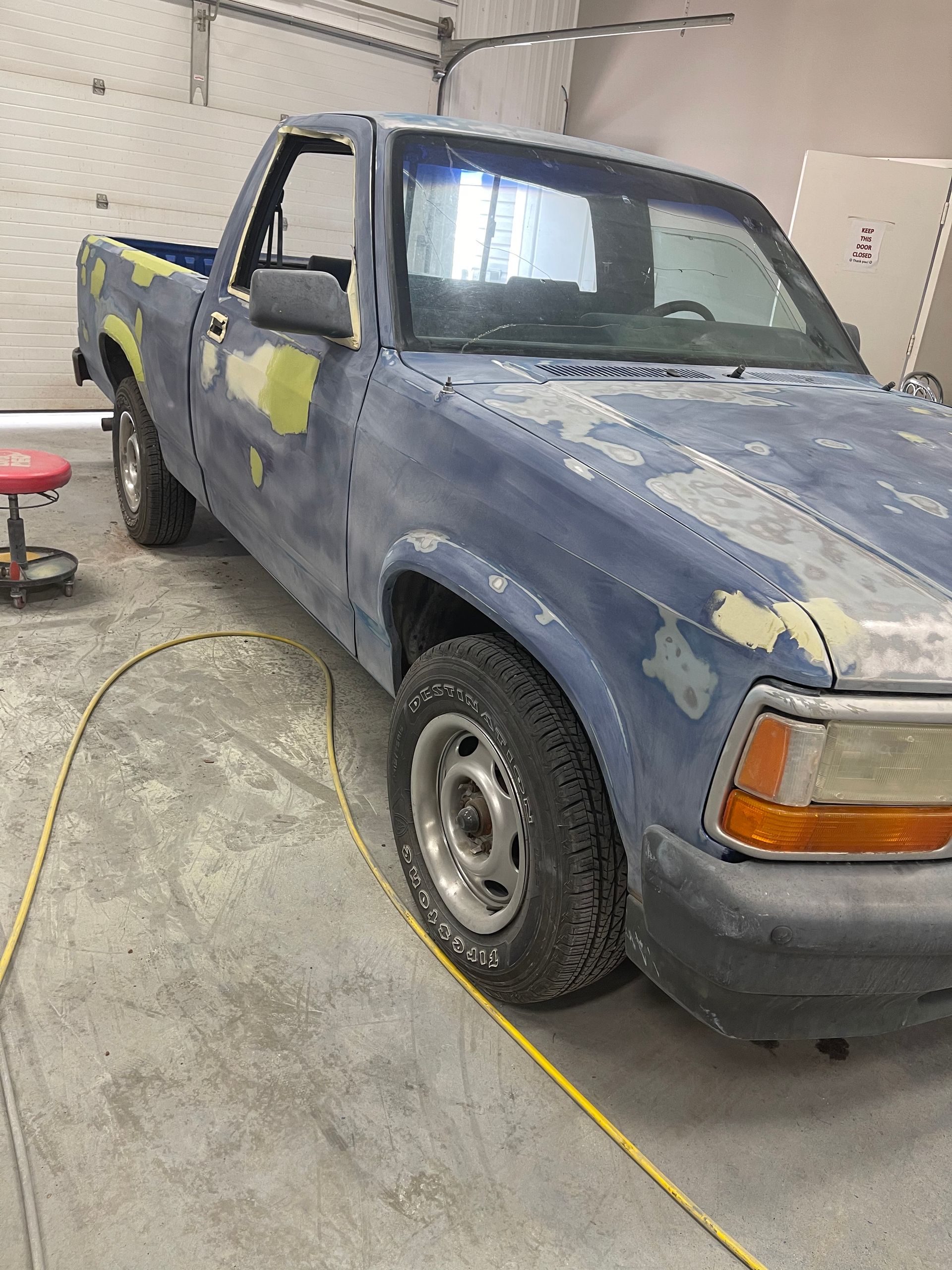A blue truck is parked in a garage next to a yellow cord.