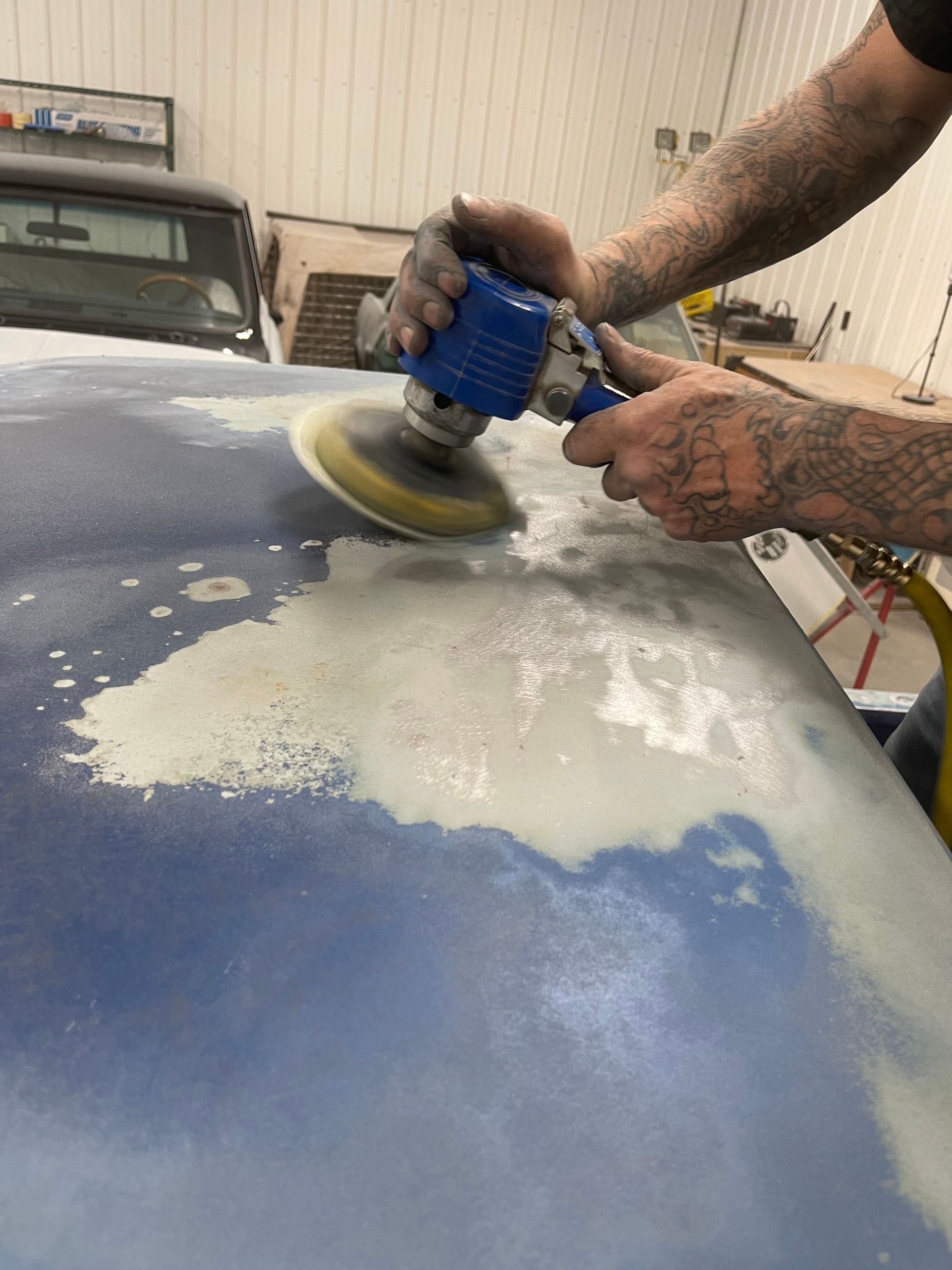 A man is polishing the hood of a car with a sander.