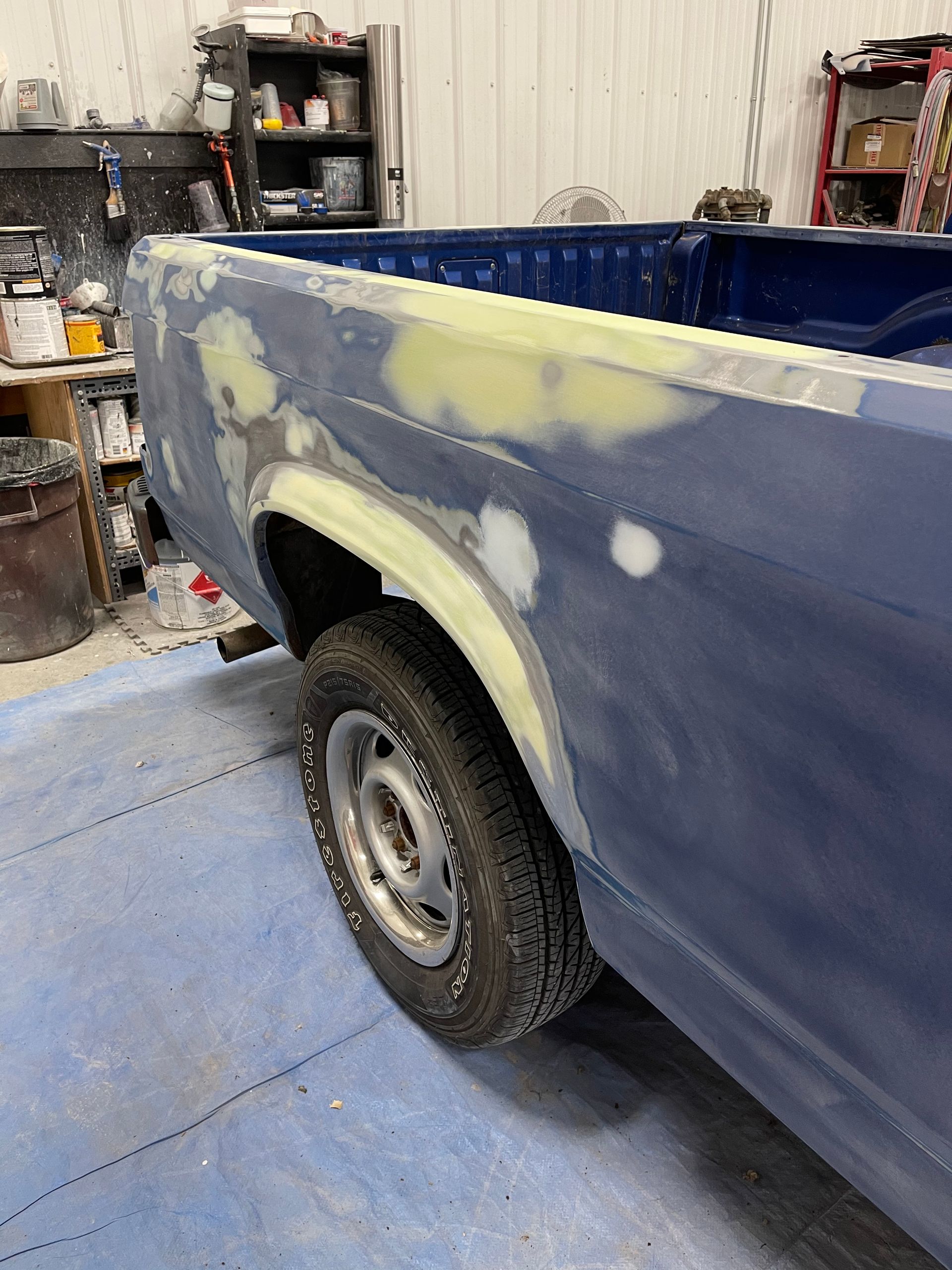 A blue truck is being painted in a garage.