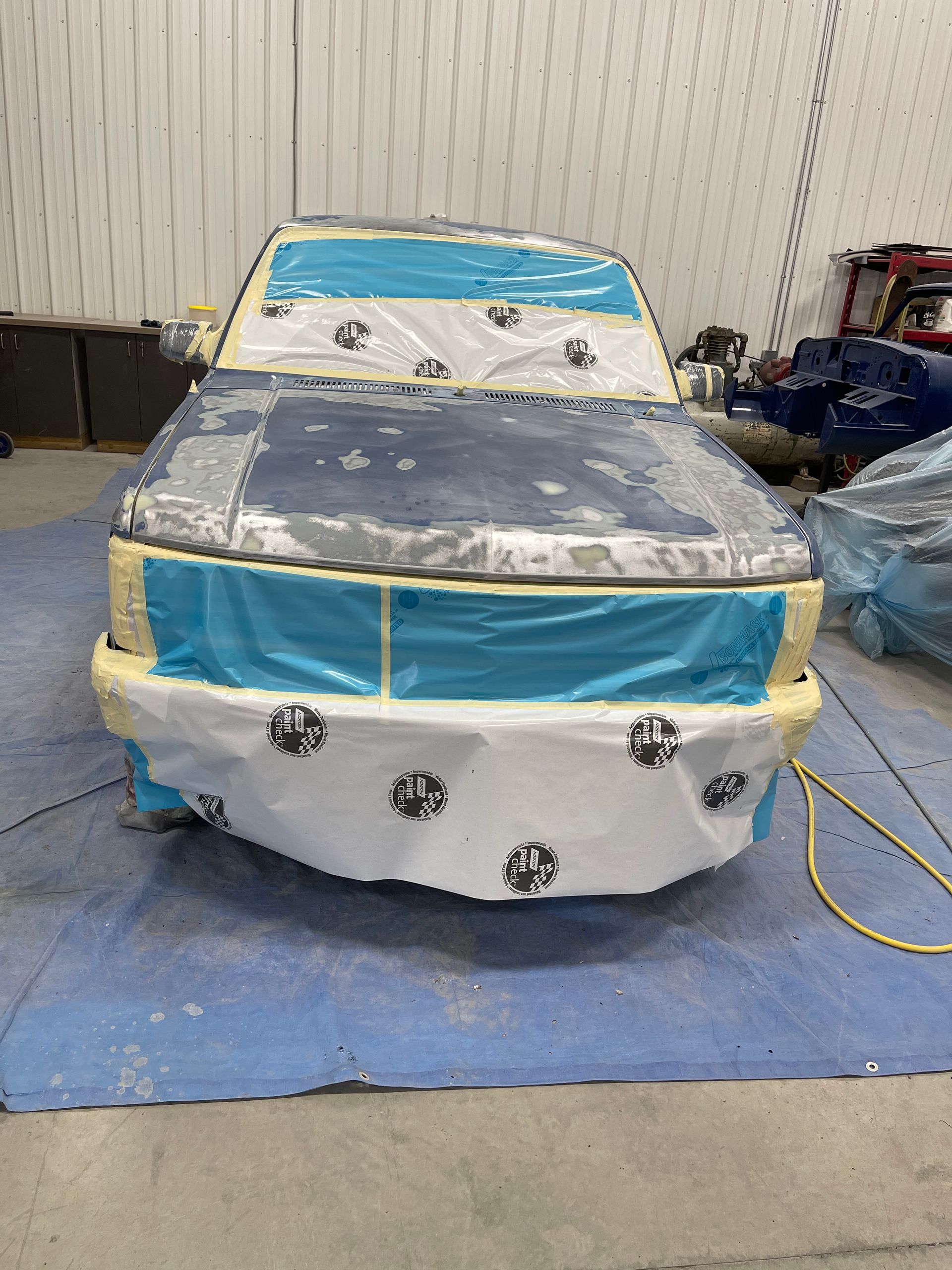 A car is being painted in a garage and is covered in plastic.