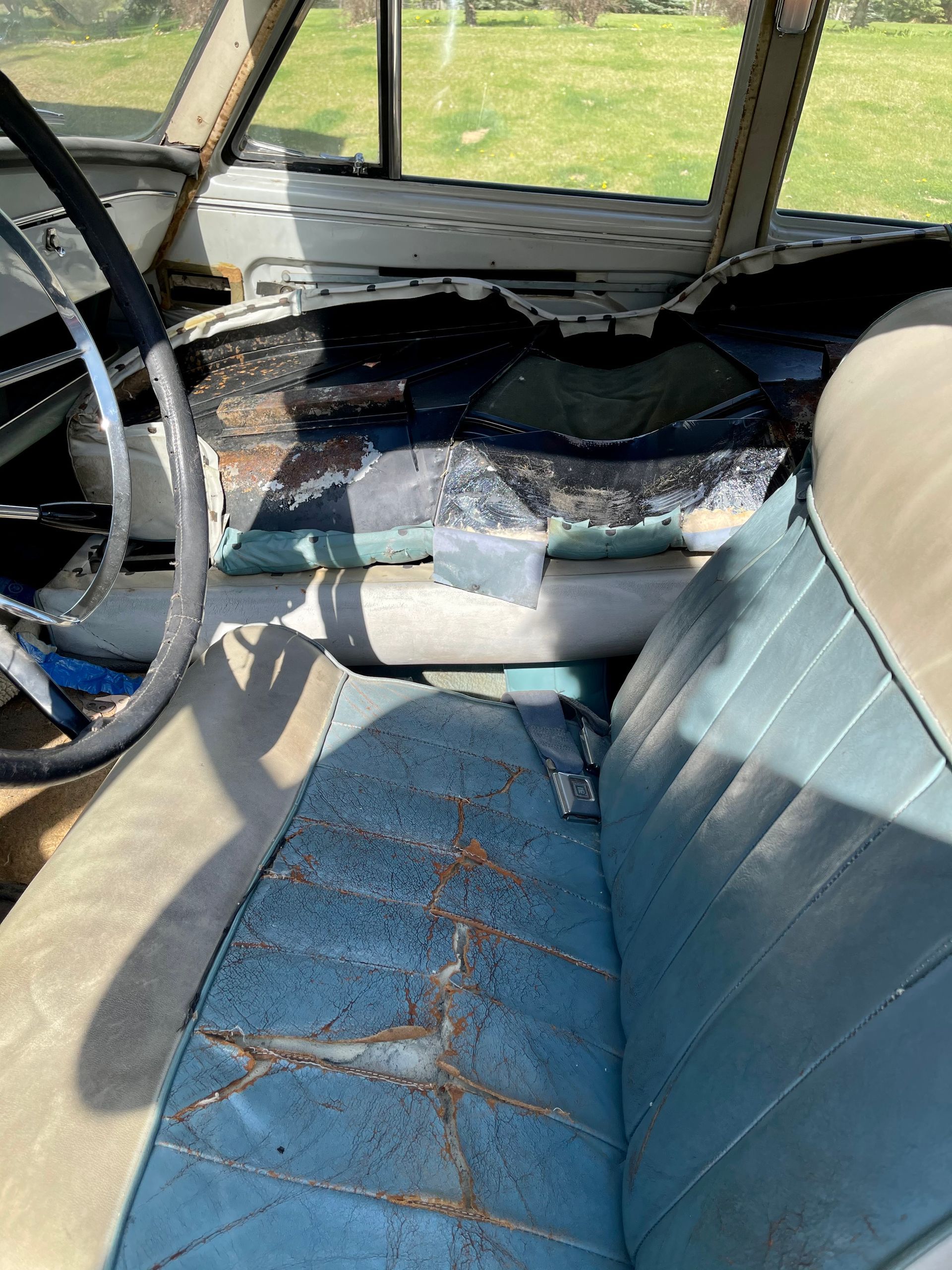 The inside of an old car with a broken seat and steering wheel.