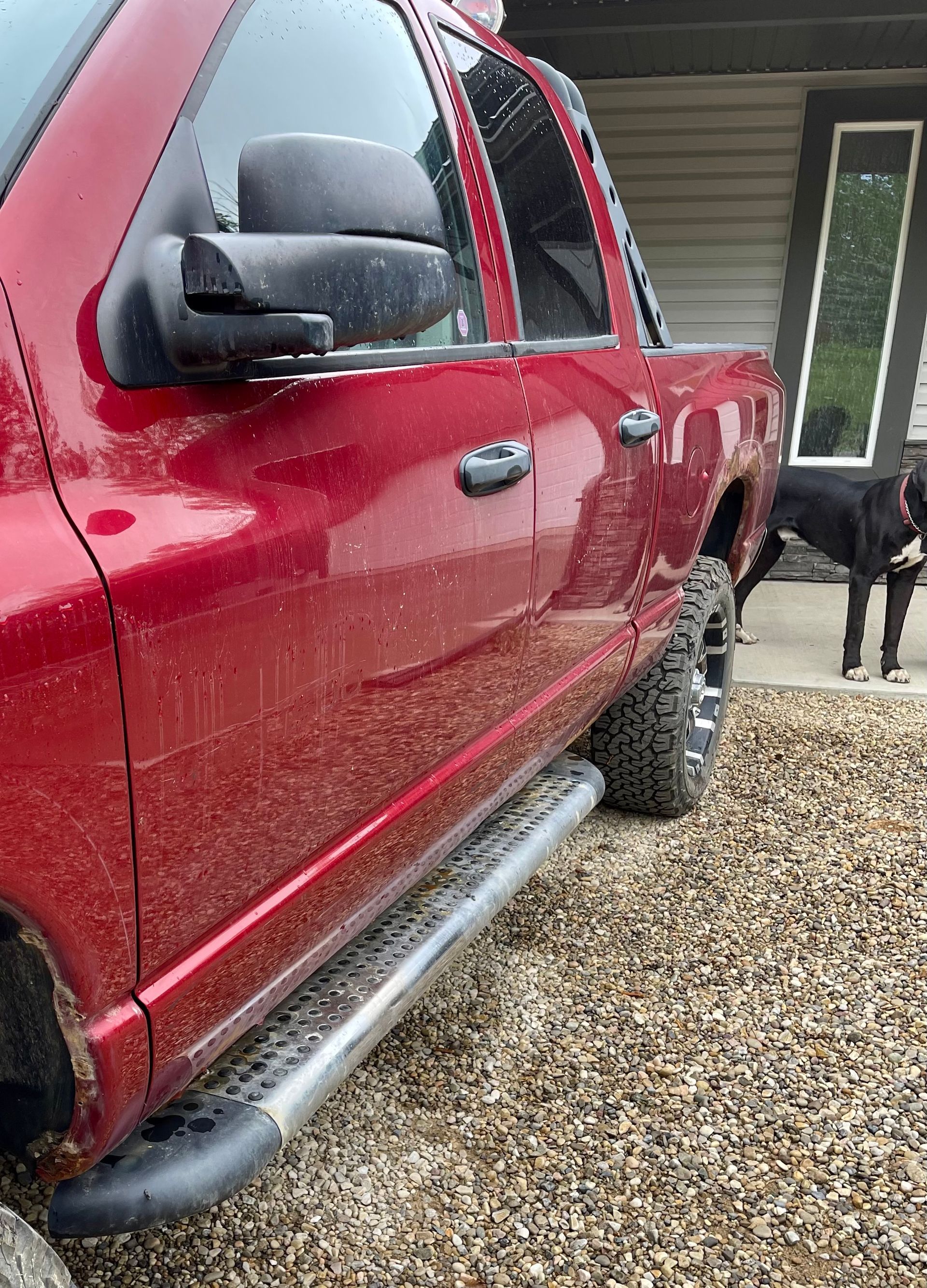 A red truck is parked in a gravel lot next to a dog.