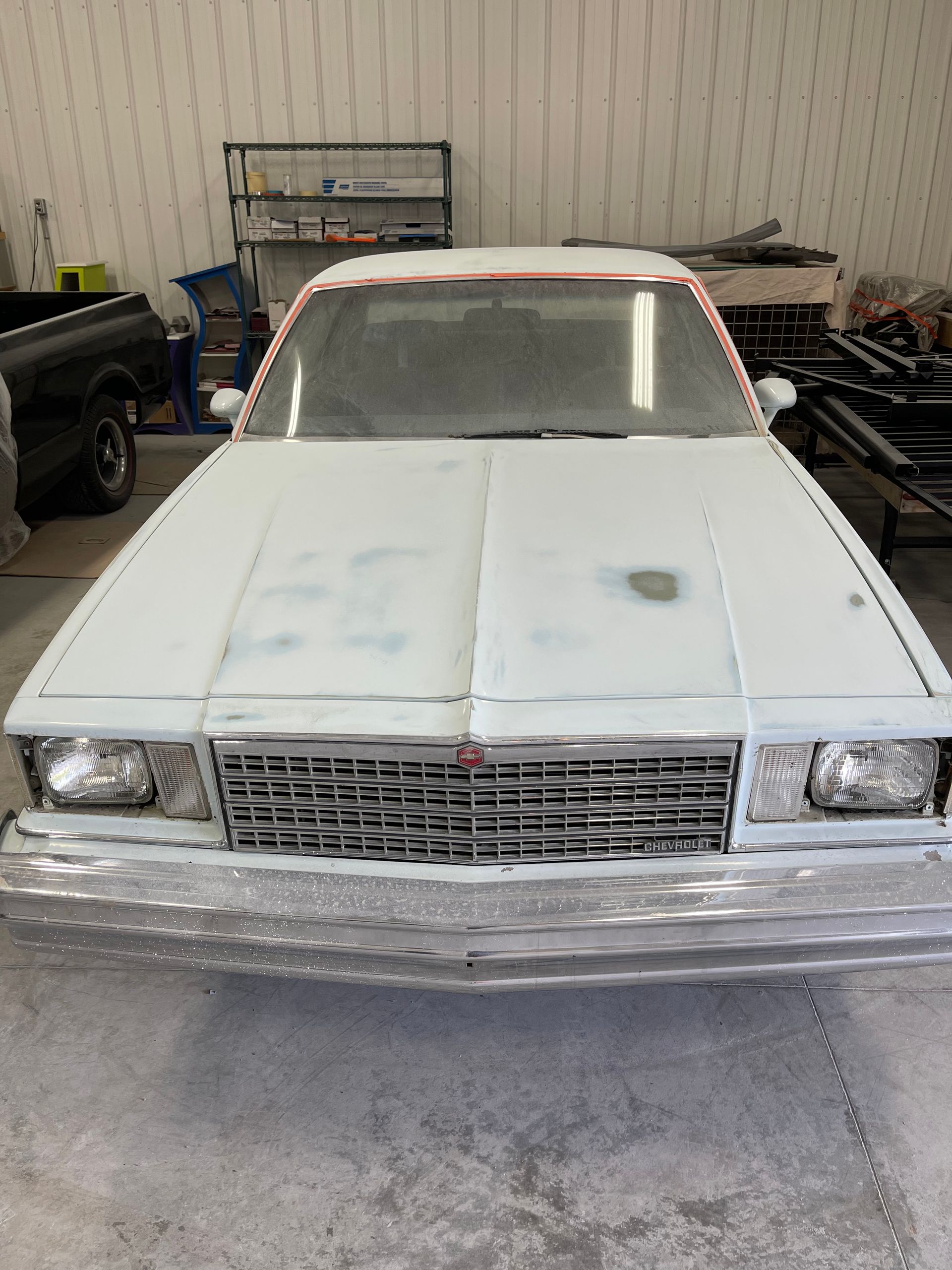 A white car is parked in a garage with a truck in the background.