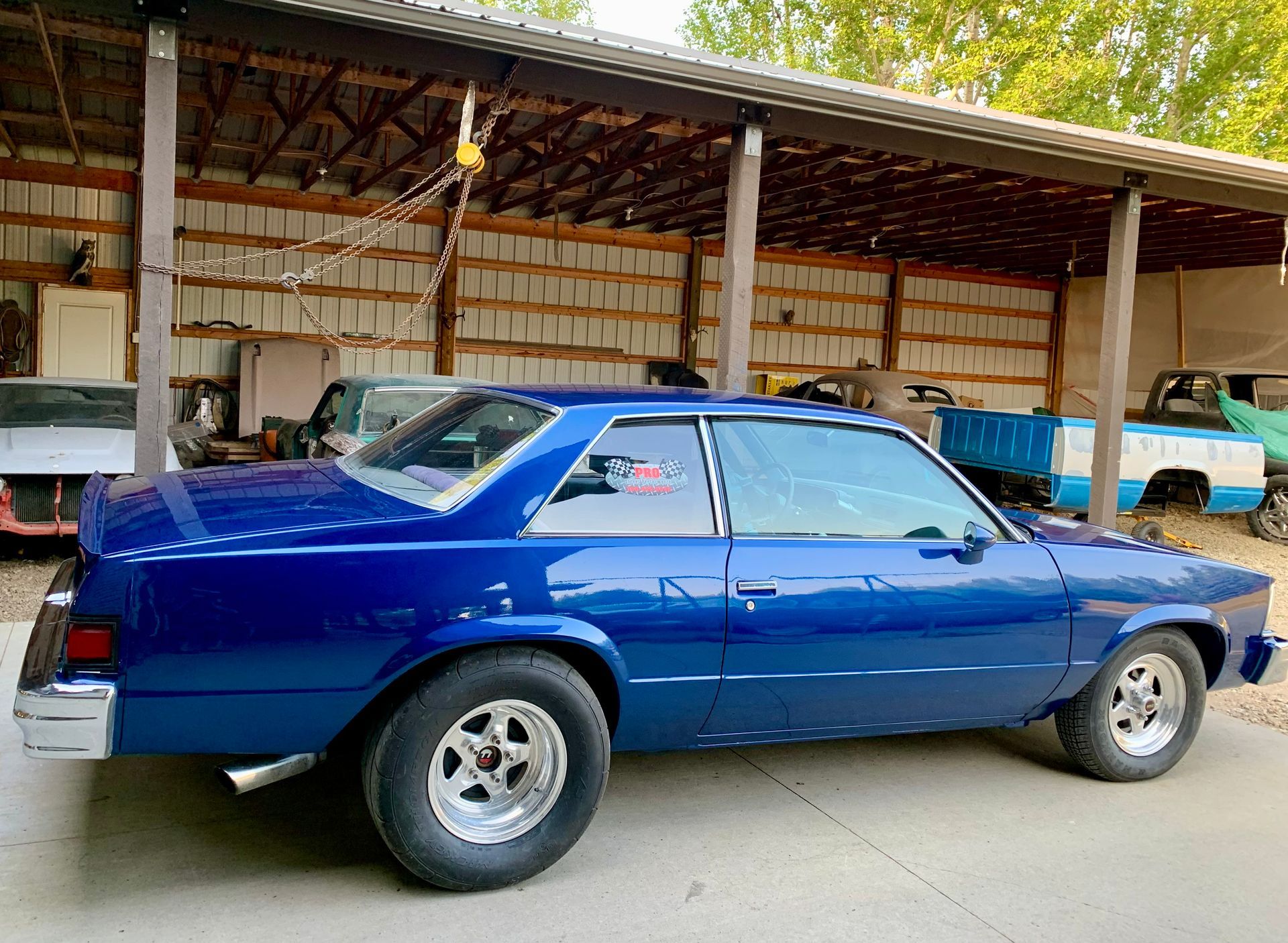 A blue car is parked in front of a barn.