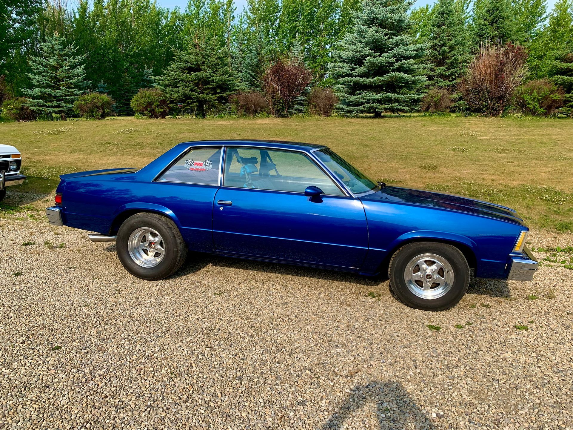 A blue car is parked in a gravel lot.
