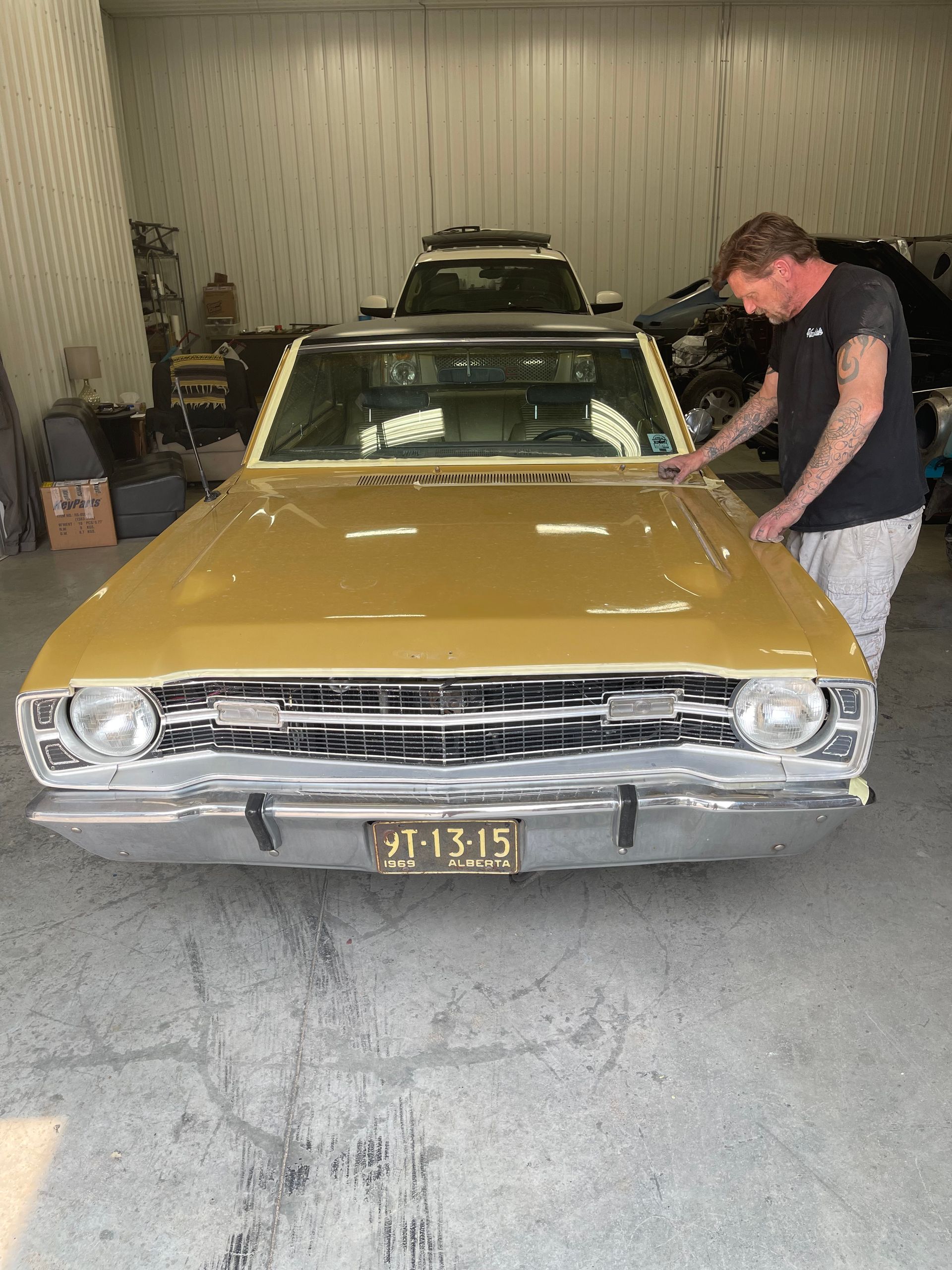 A man is standing next to a yellow car in a garage.