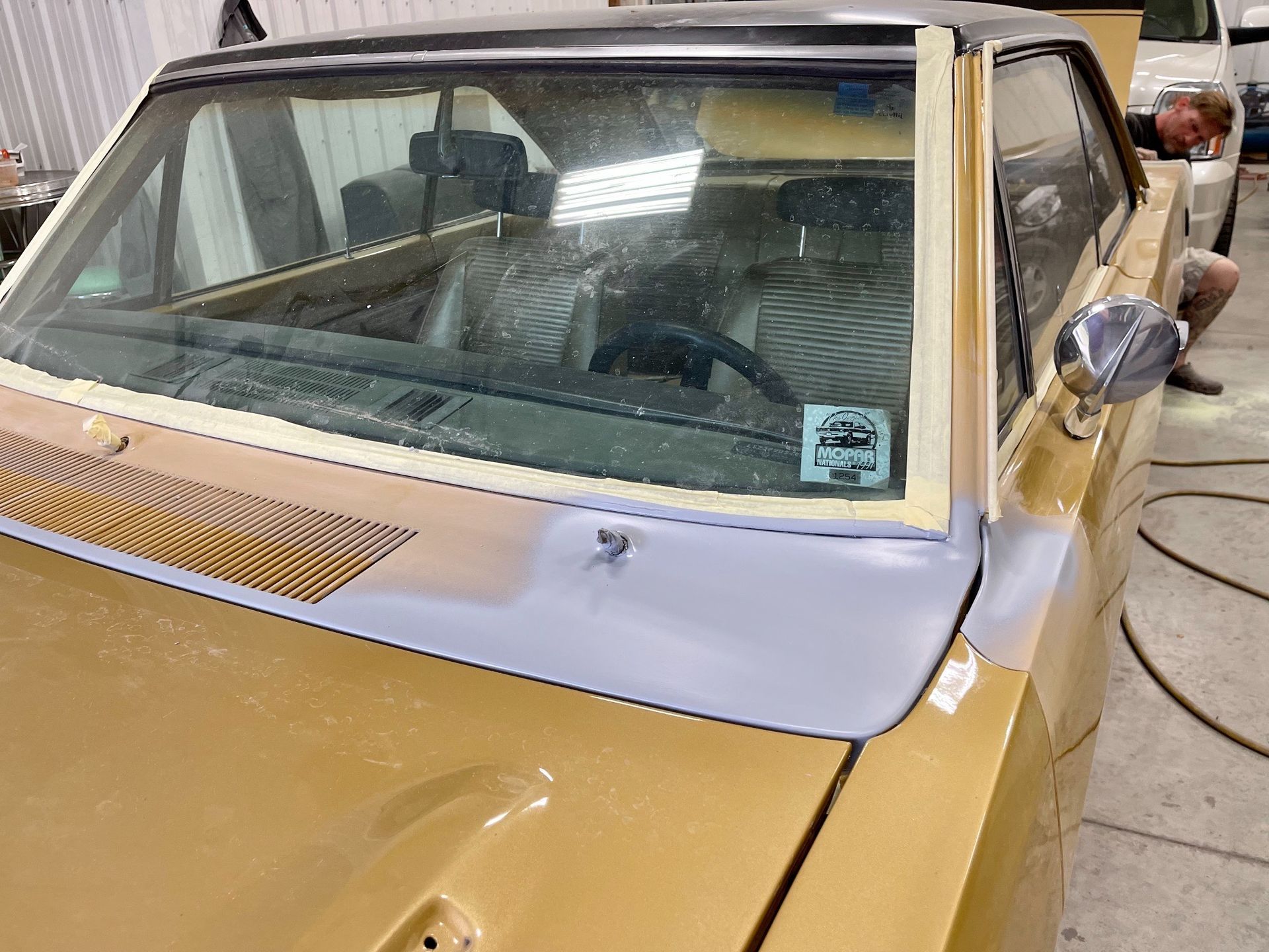 A gold car is being painted in a garage.