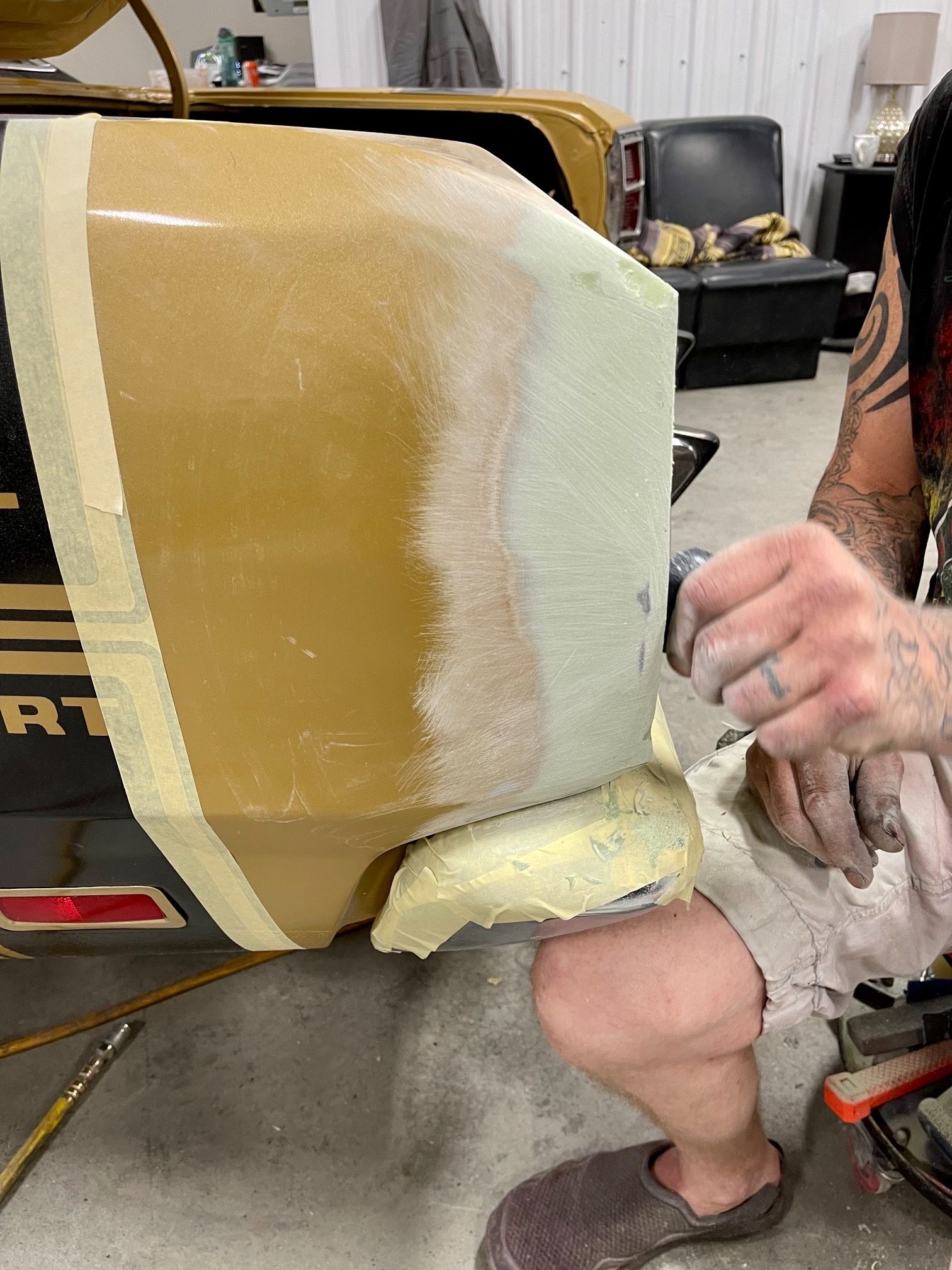 A man is sanding the side of a car with a sander.