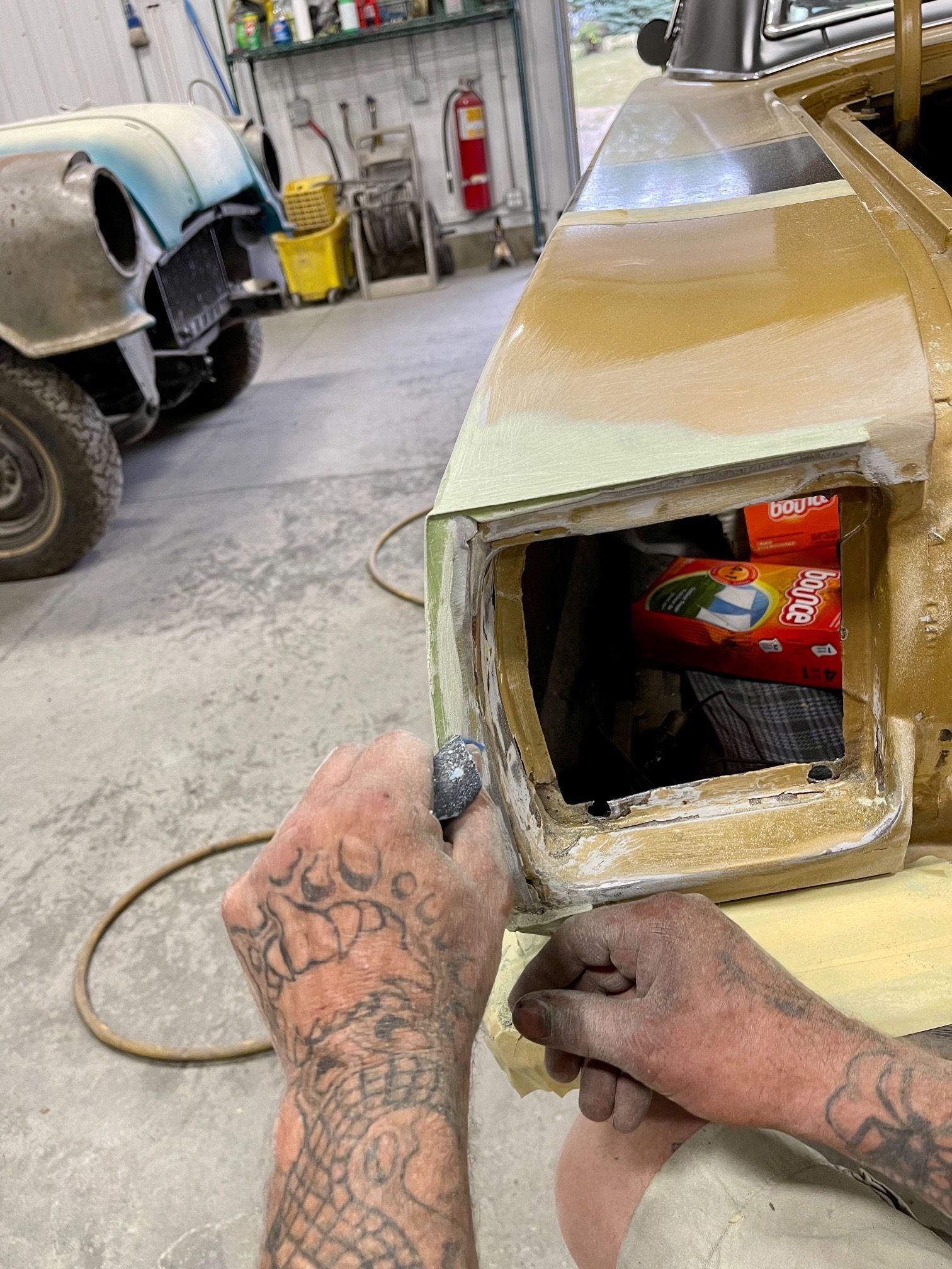 A man with tattoos is working on a car in a garage.