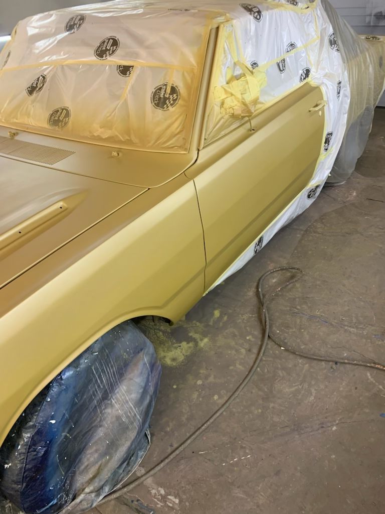 A yellow car is being painted in a garage.