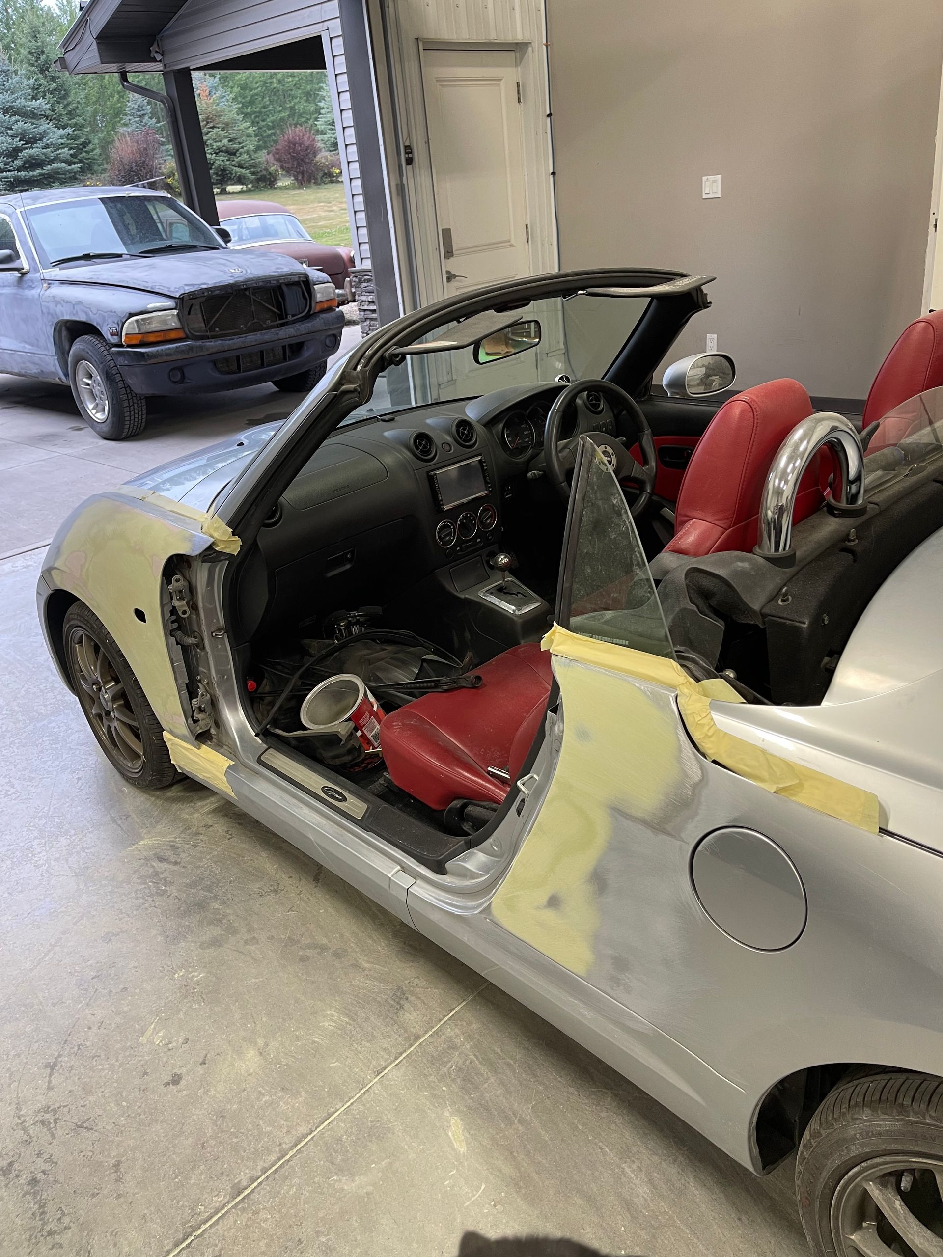 A silver convertible with red seats is sitting in a garage.