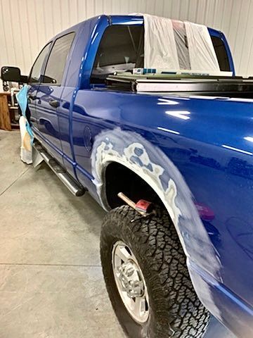 A blue truck is being painted in a garage.