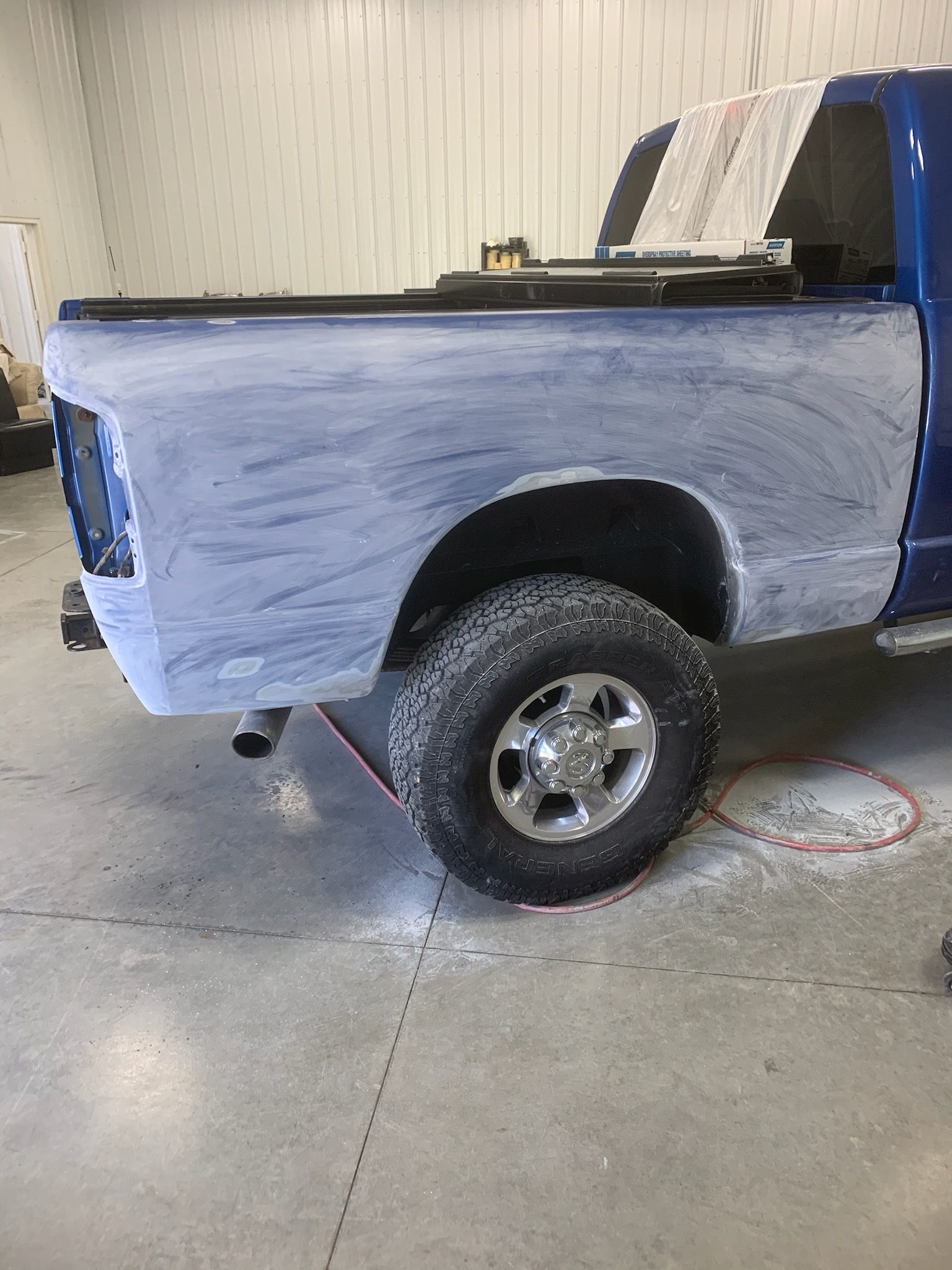 A blue truck is being painted in a garage.