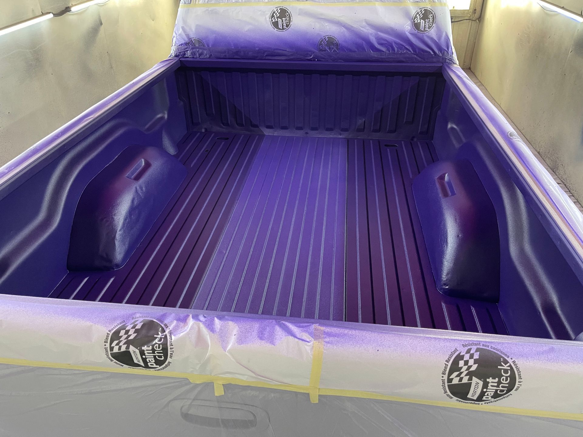 The bed of a purple truck is being painted.