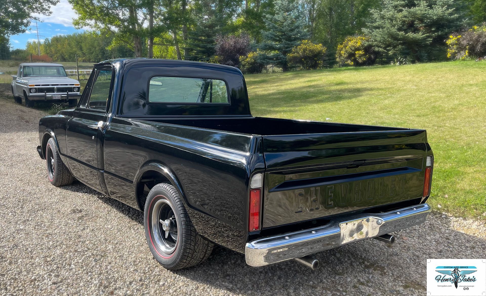 A black truck is parked on a gravel road next to a grassy field.