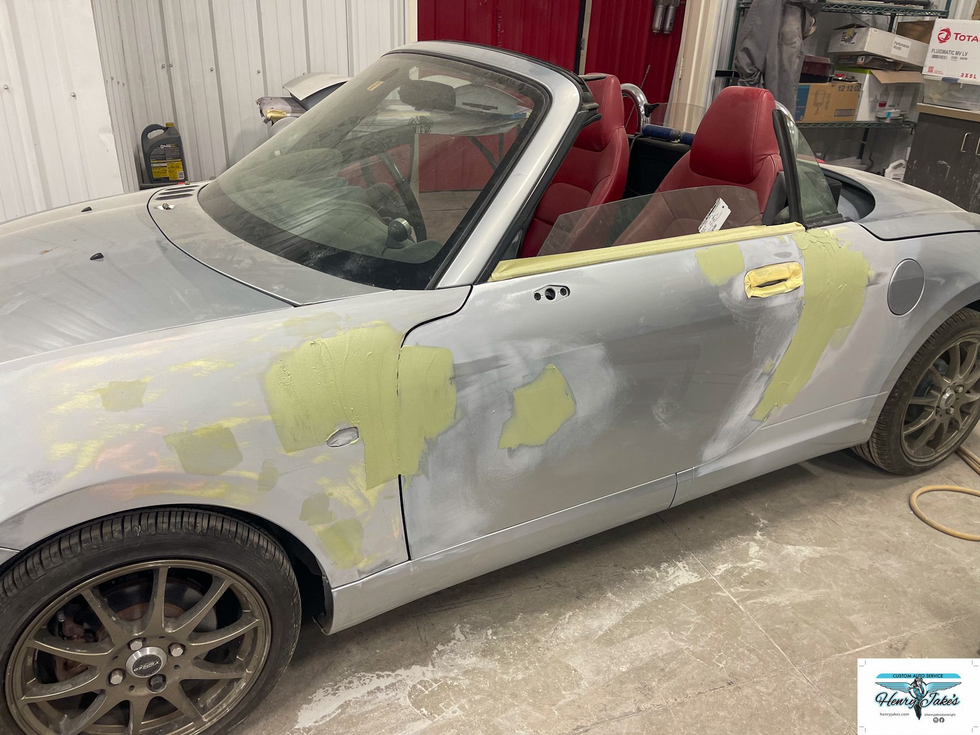 A silver convertible with red seats is being painted in a garage.