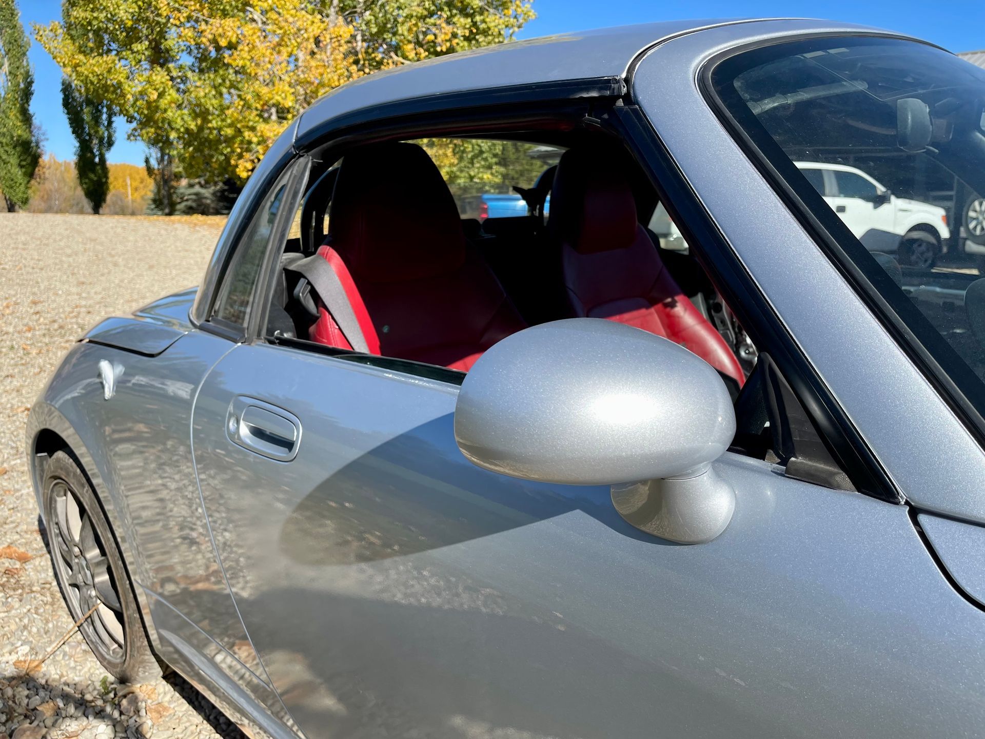 A silver sports car with red seats is parked in a field.