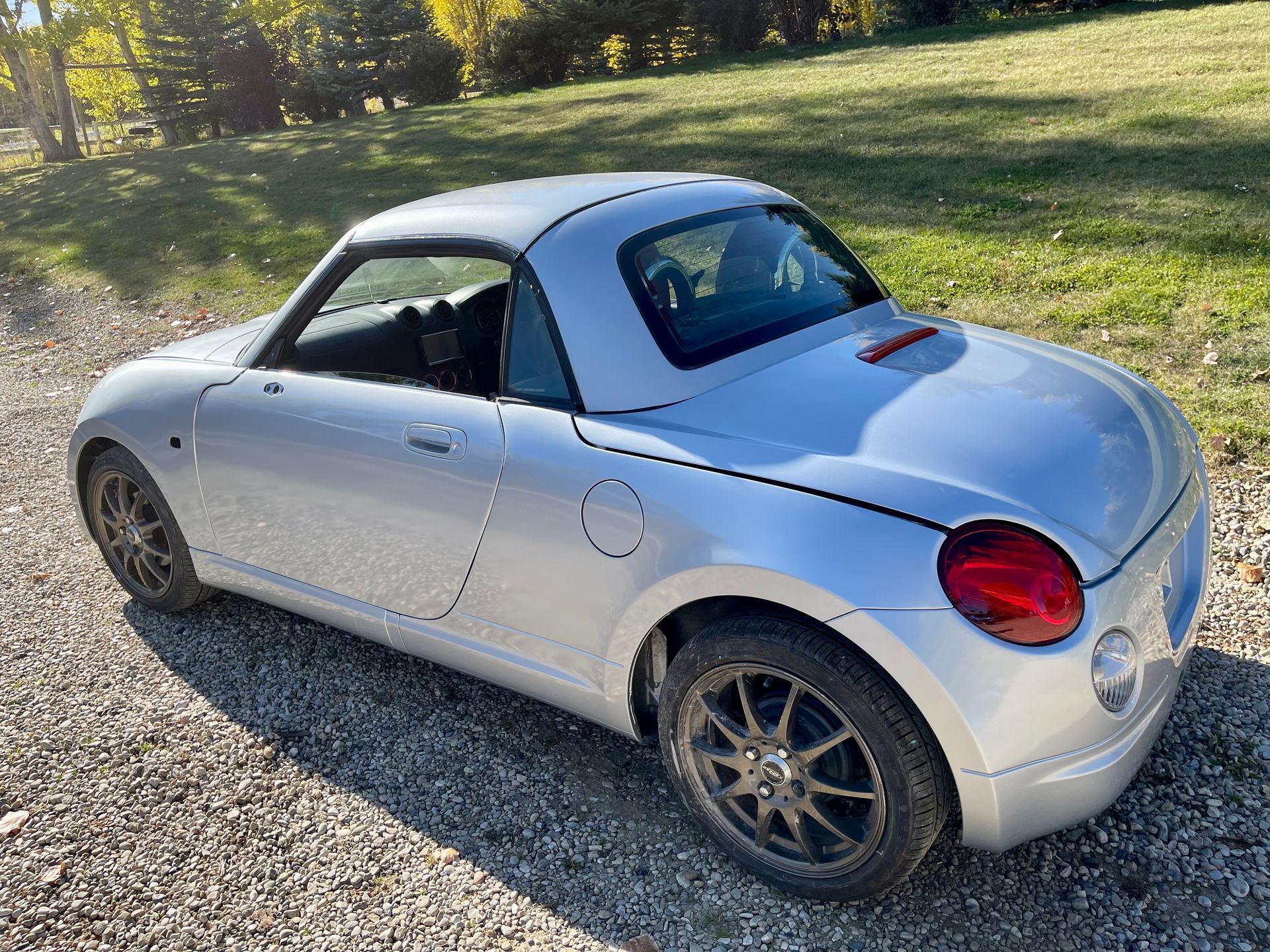 A silver convertible car is parked on a gravel road.