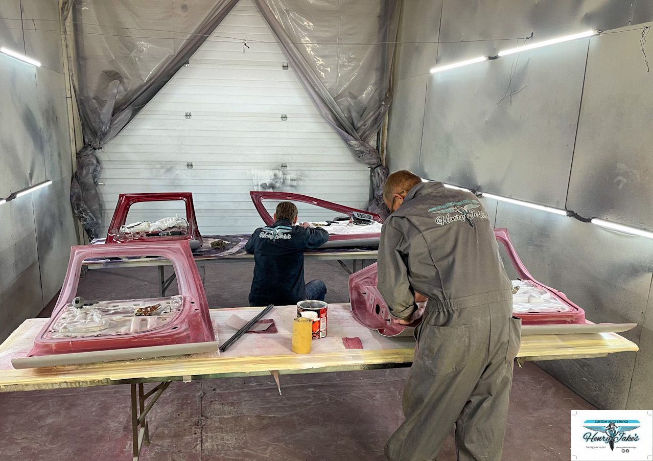 Two men are working on a red car in a paint booth.