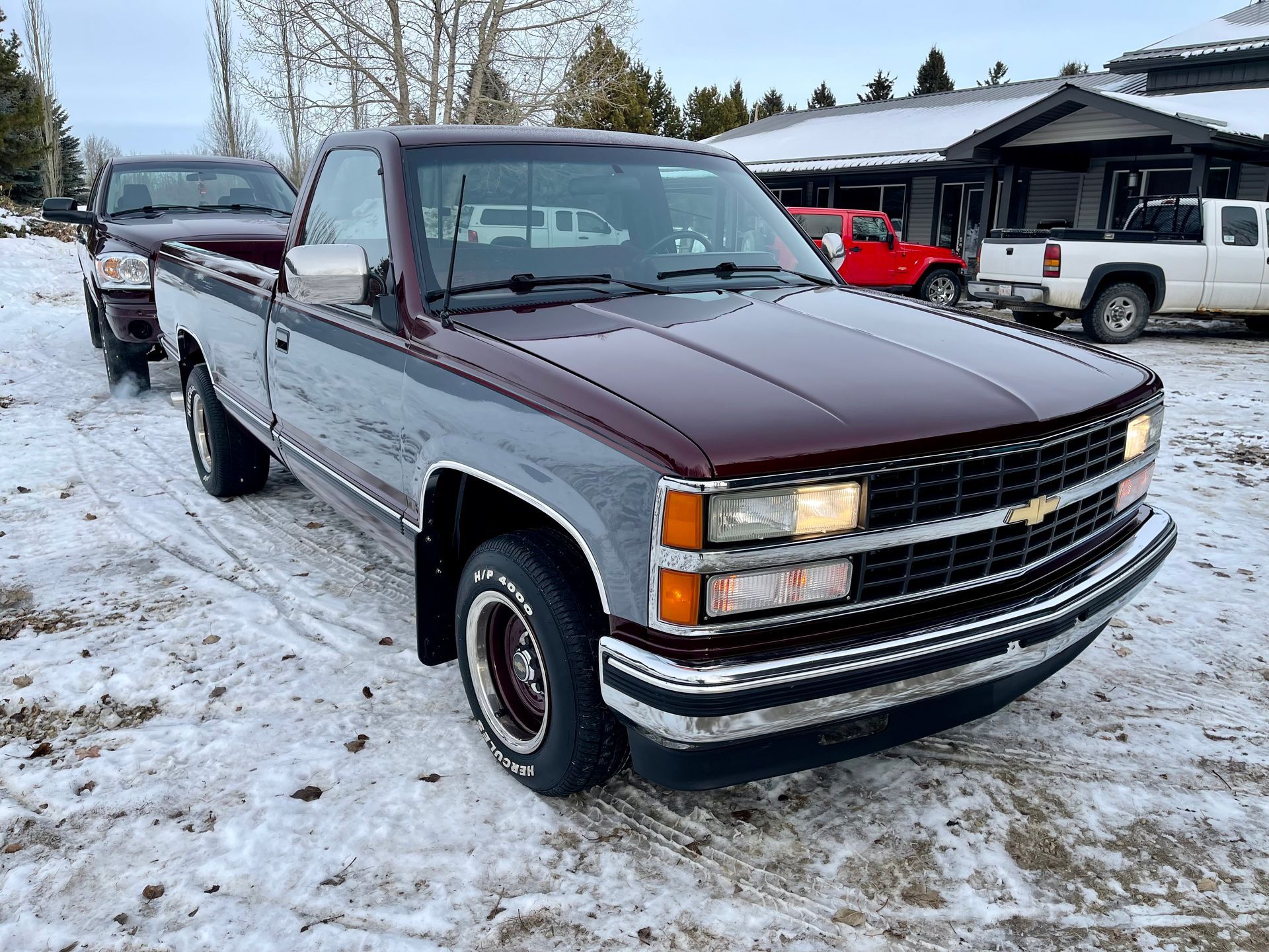 A pickup truck is parked in the snow in front of a house.