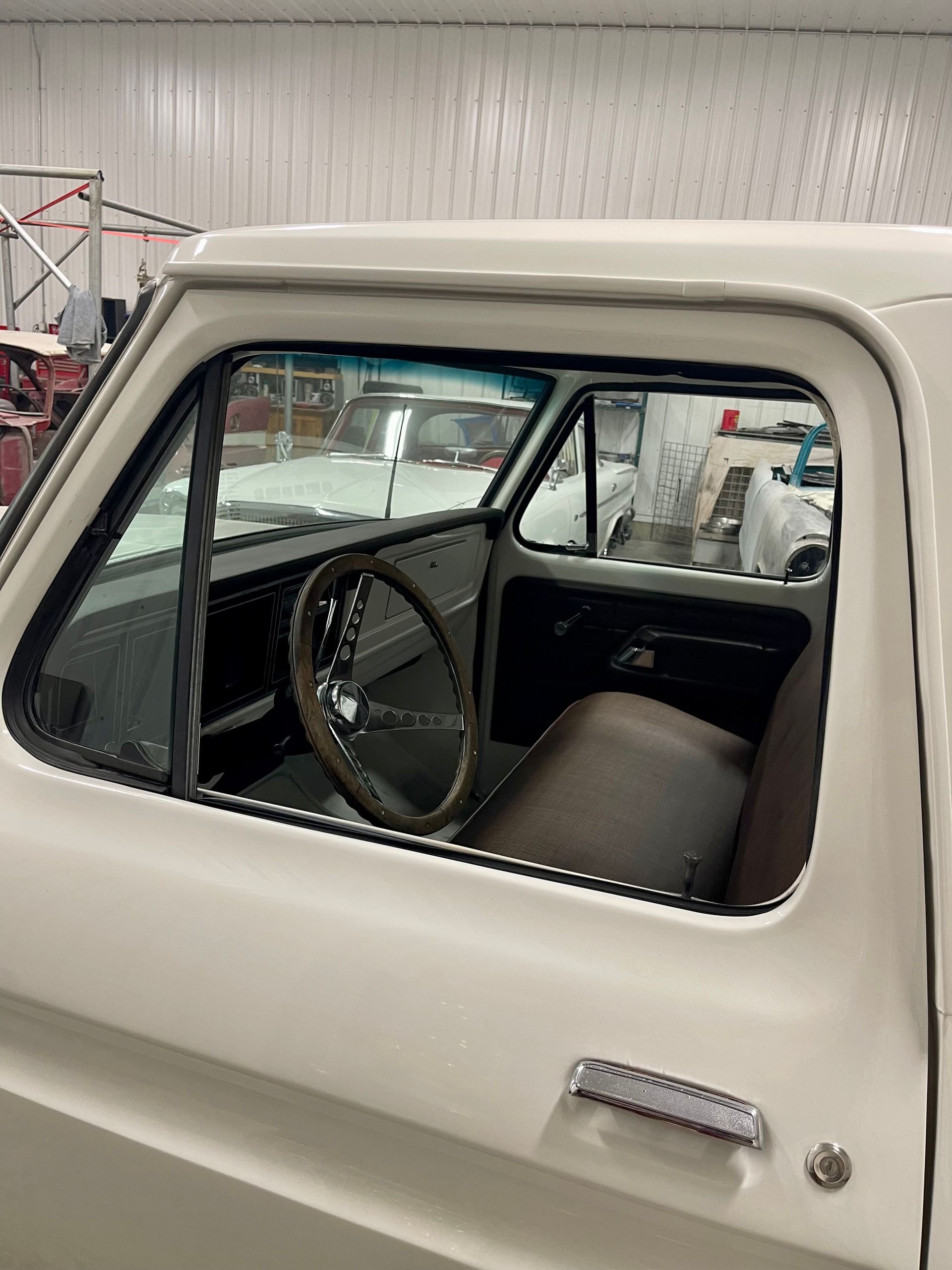 A white truck with a brown seat and steering wheel is parked in a garage.