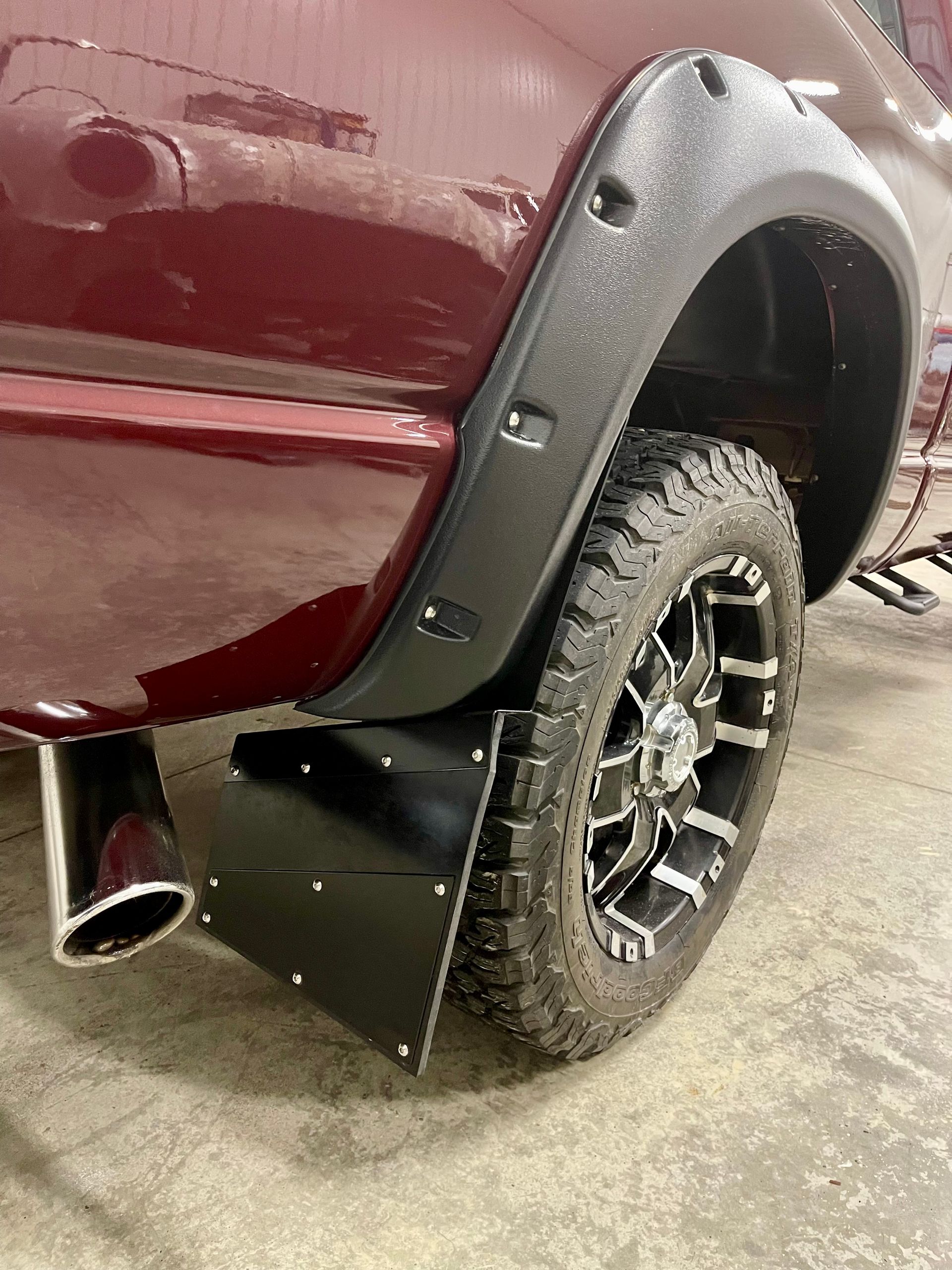 A red truck with mud flaps and fender flares is parked in a garage.