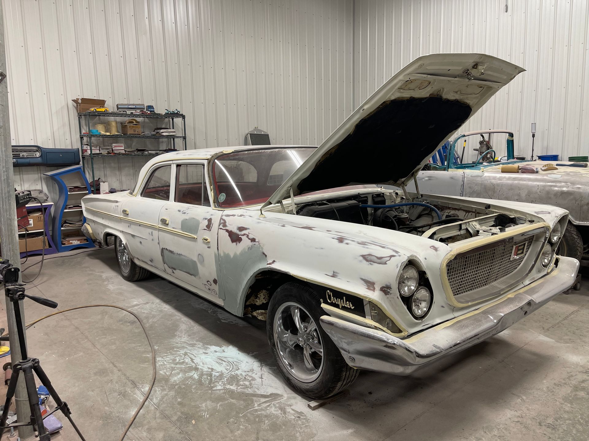 A white car with the hood up is sitting in a garage.